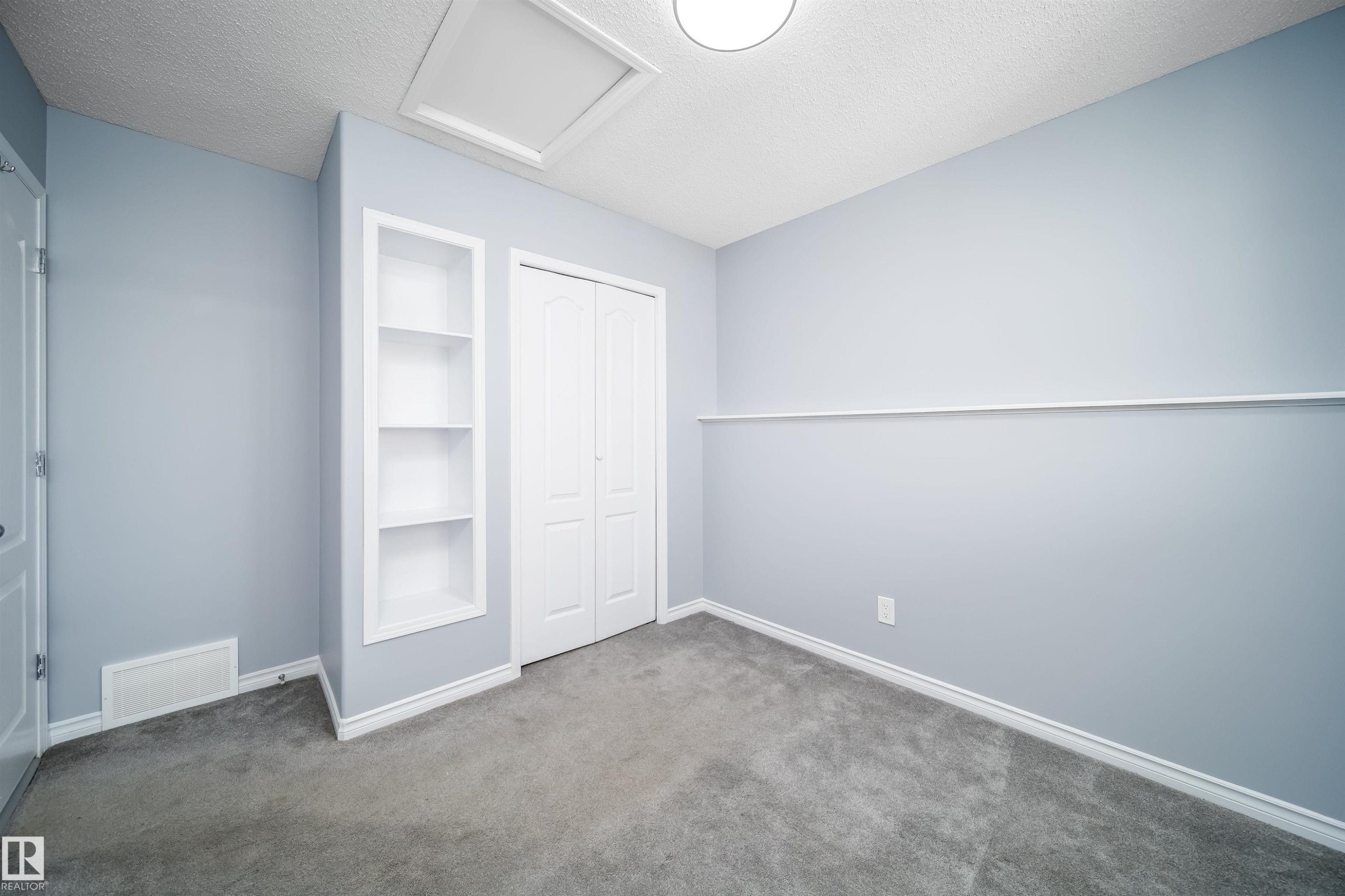 Gray carpeted flooring, light blue walls, built-in shelving, bi-fold closet doors, and recessed ceiling lighting - 7848 7 Avenue Sw, Edmonton, AB