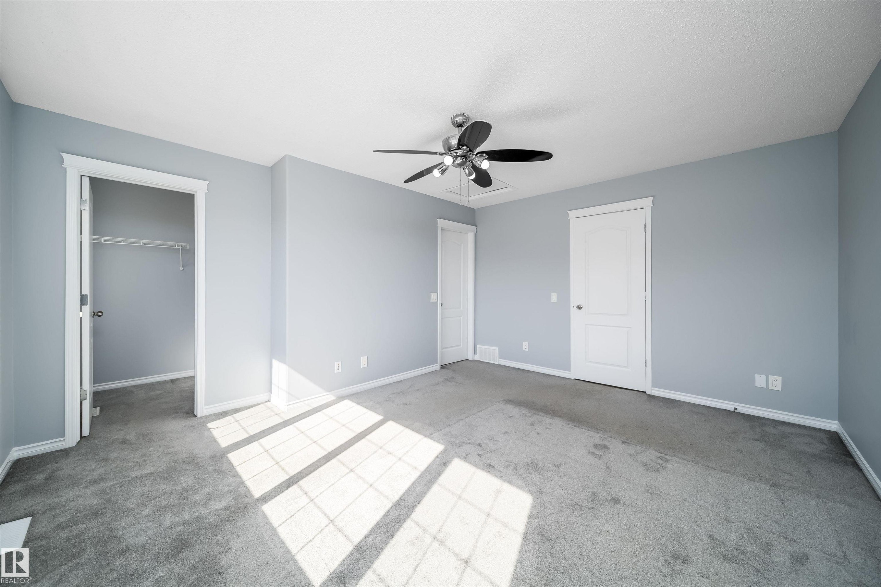 Spacious interior room with light blue walls, gray carpet flooring, and a ceiling fan with integrated lighting - 7848 7 Avenue Sw, Edmonton, AB