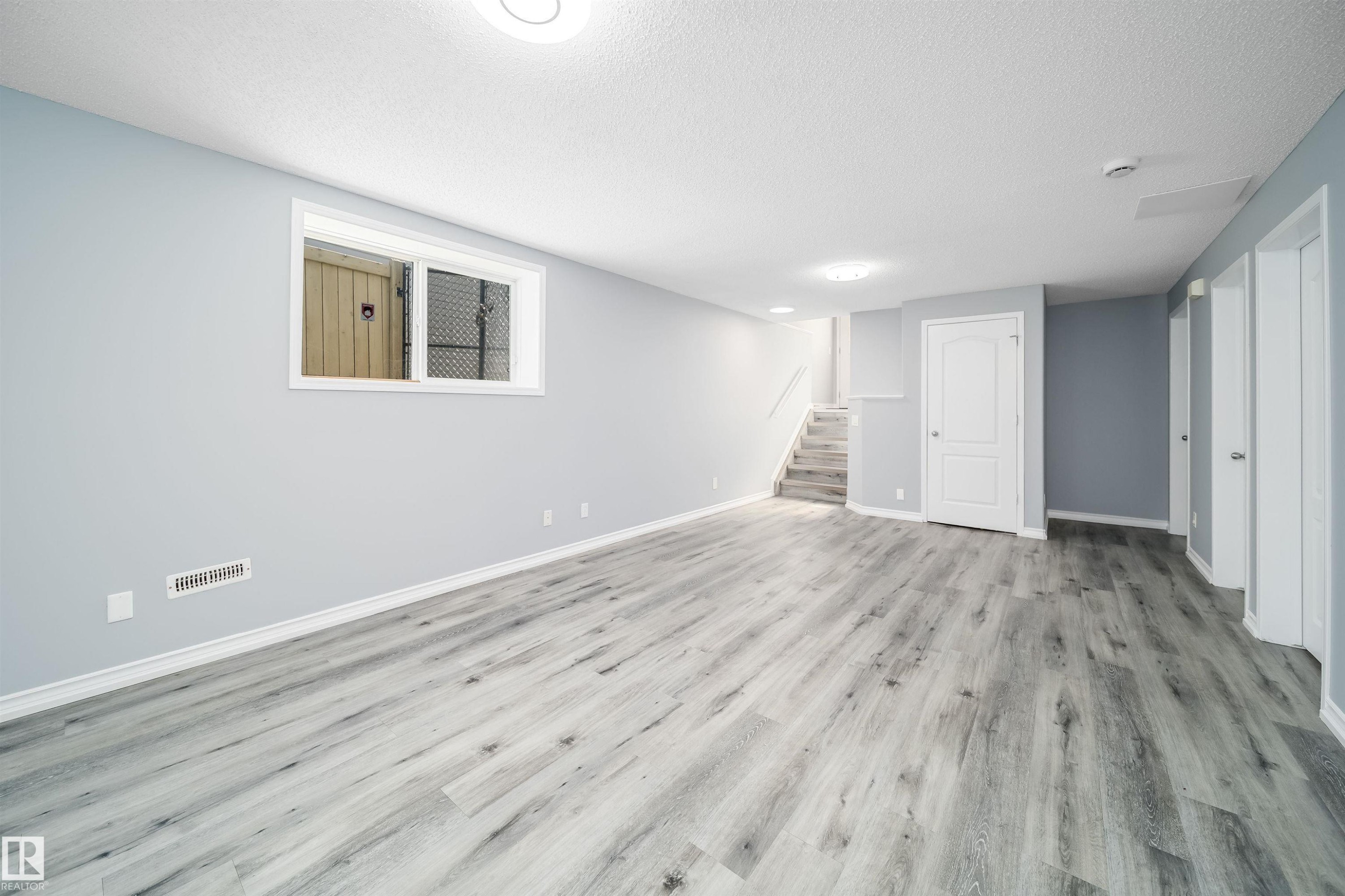 Expansive open area with wood-finish flooring, recessed lighting, and a window with security bars - 7848 7 Avenue Sw, Edmonton, AB
