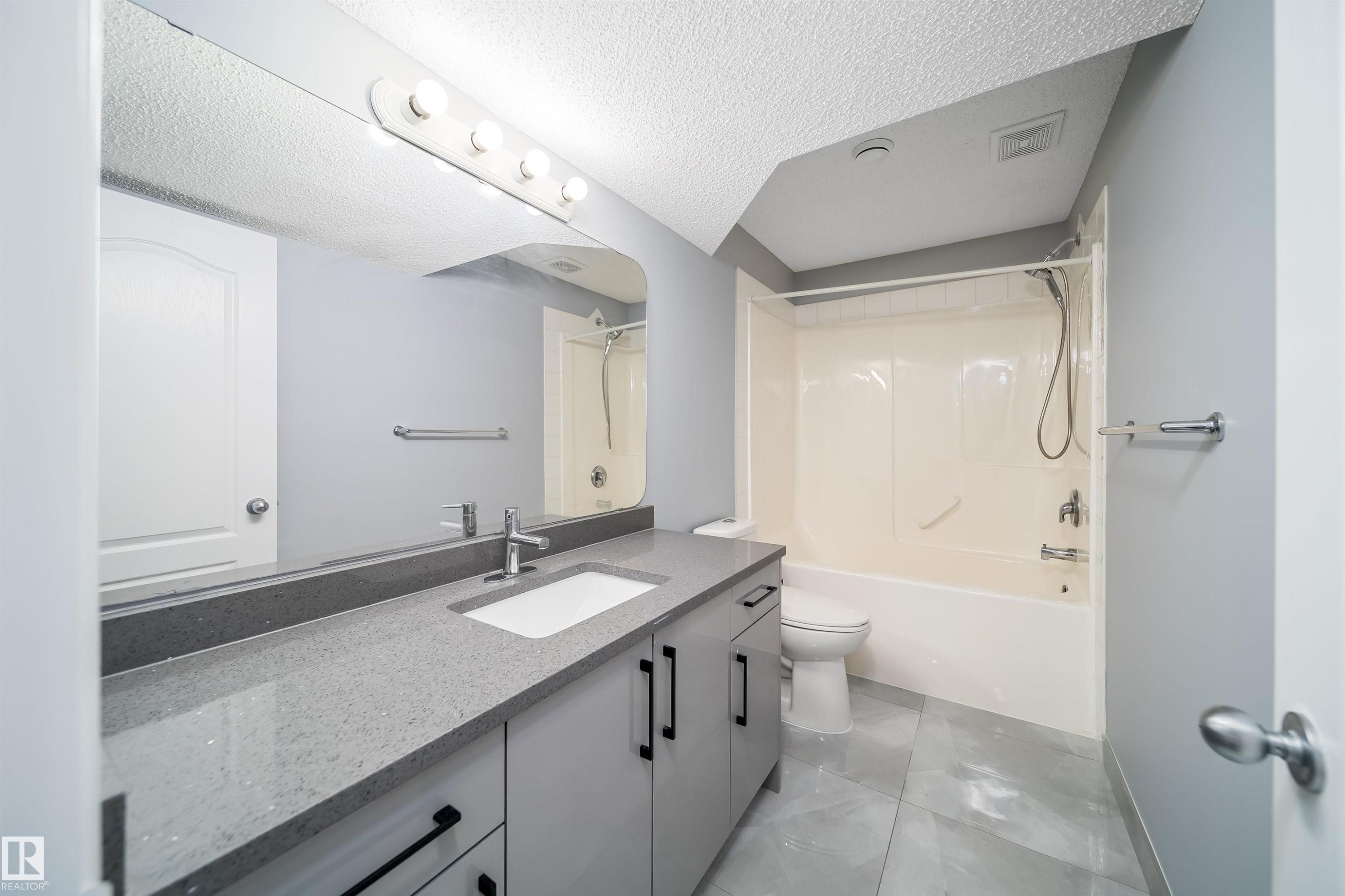 Spacious bathroom featuring a single vanity with stone-finish countertop, integrated sink, and contemporary cabinetry with black hardware - 7848 7 Avenue Sw, Edmonton, AB