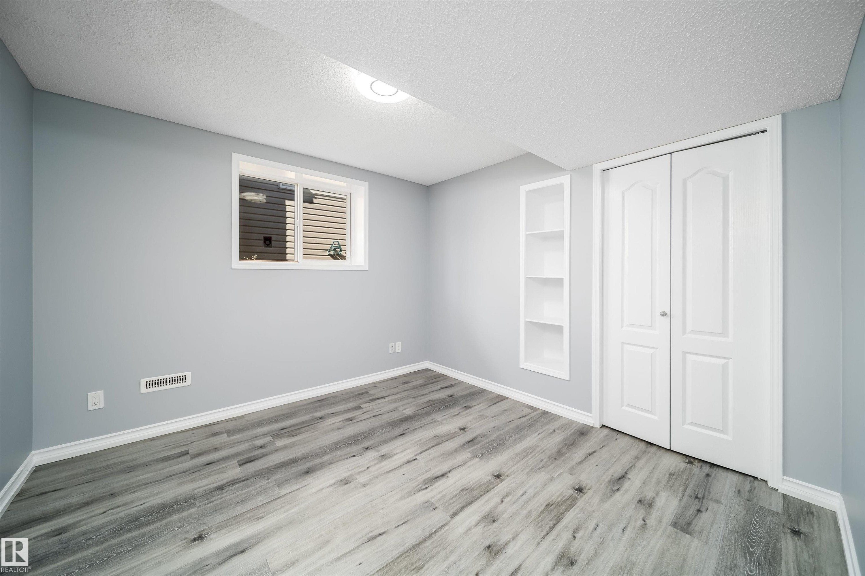 Wood-finish flooring, recessed built-in shelving, white bi-fold closet doors, and a window with white trim - 7848 7 Avenue Sw, Edmonton, AB