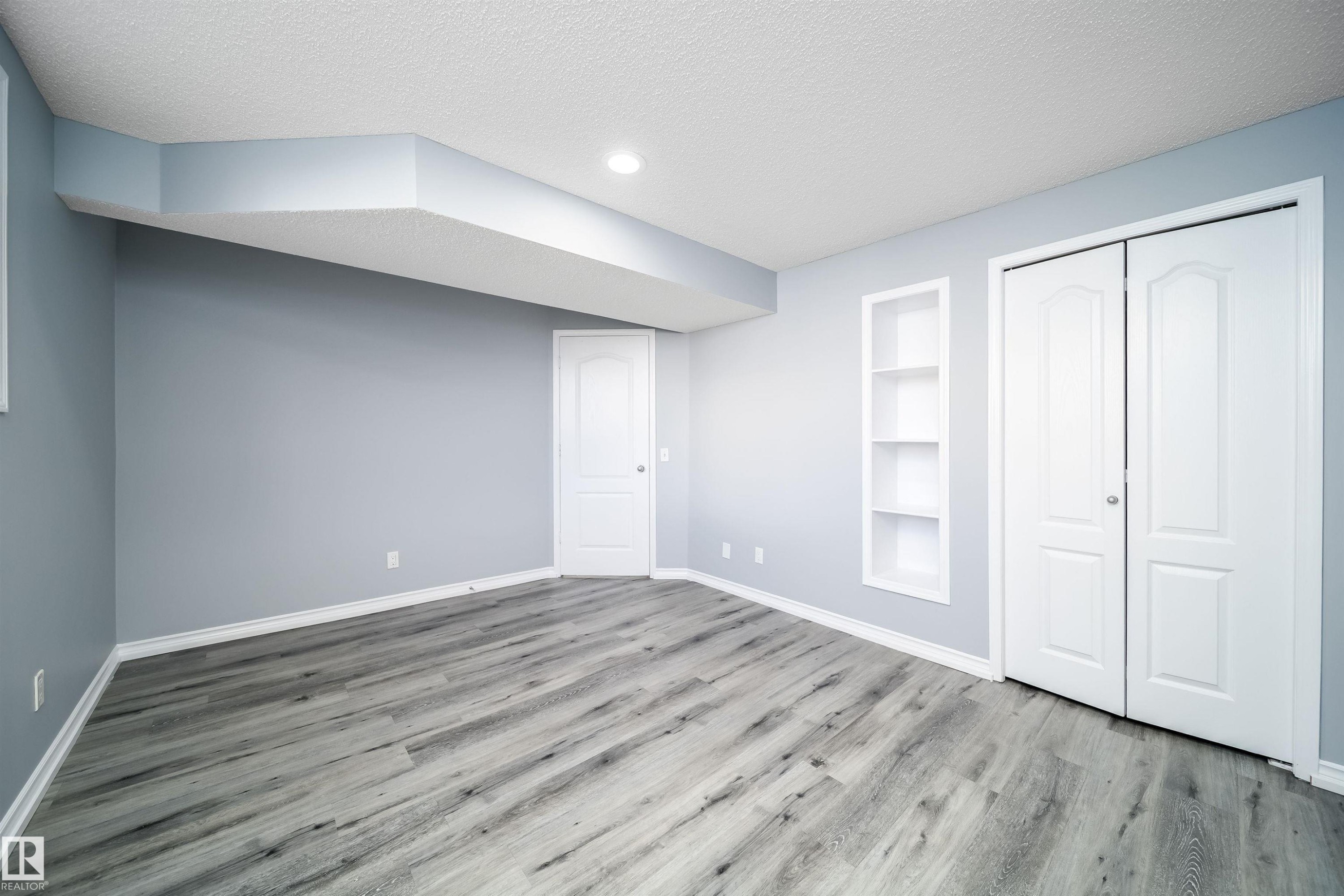Recessed lighting illuminates the wood-finish flooring, complemented by a built-in shelving unit and two panel doors - 7848 7 Avenue Sw, Edmonton, AB