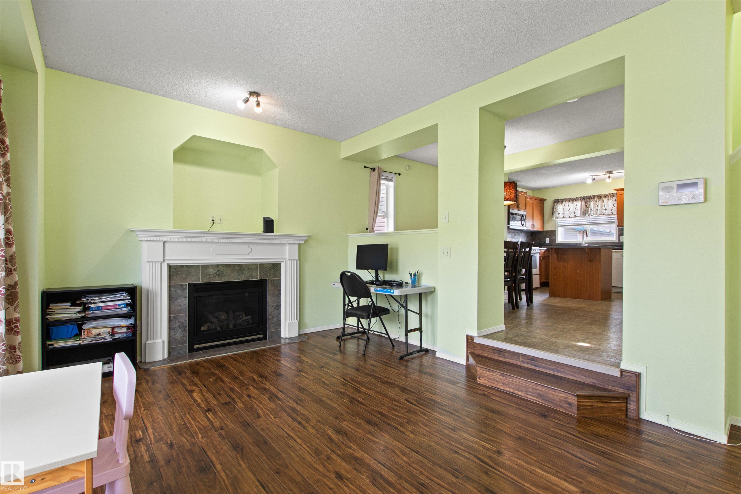 Wood-finish flooring throughout, featuring a fireplace with a detailed white mantel and stone-tile surround - 9118 Scott Crescent Nw, Edmonton, AB - Indoor Photo Showing Living Room With Fireplace