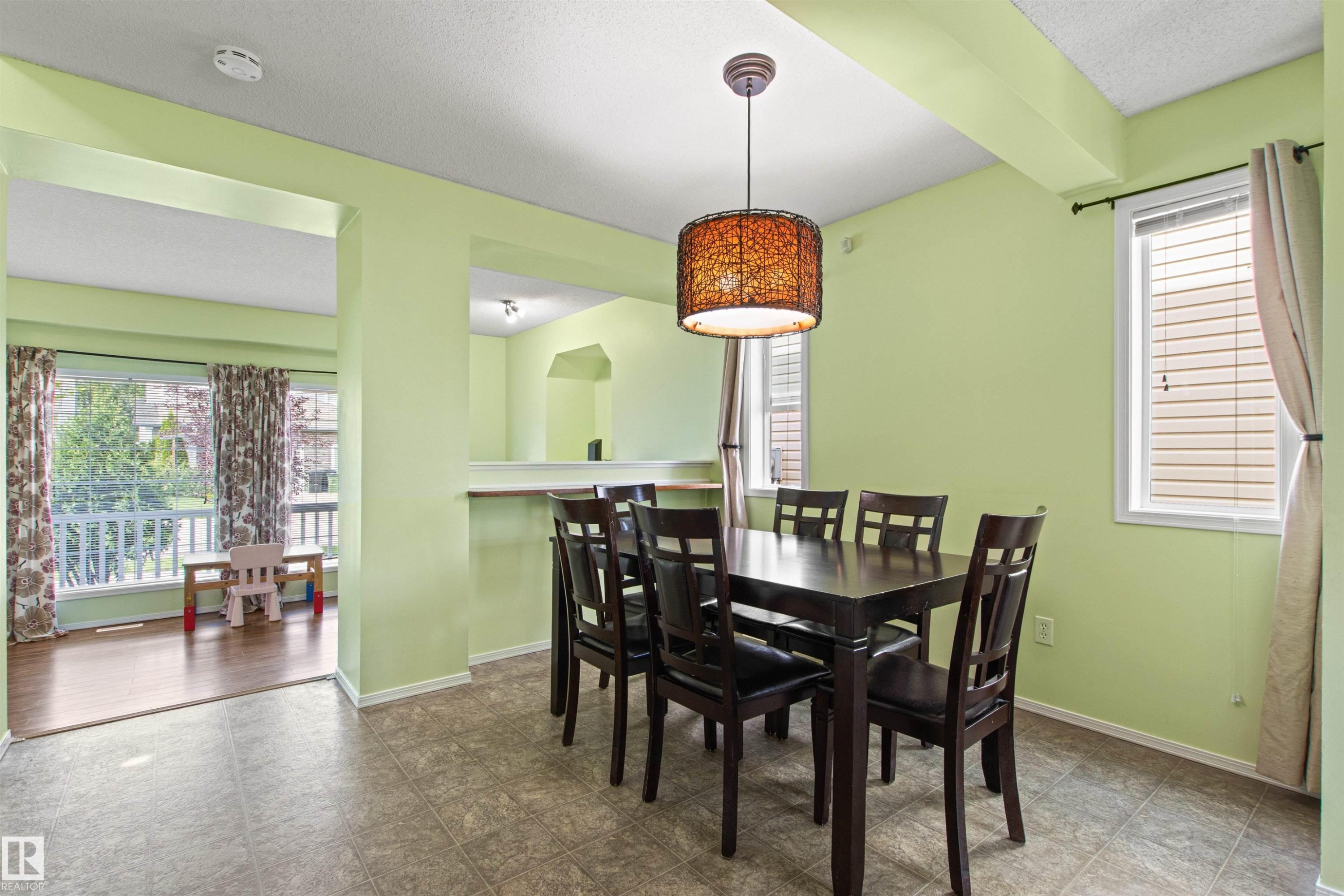 Tile flooring in the dining area with a decorative pendant light fixture, a window with blinds, and an arched pass-through to an additional space - 9118 Scott Crescent Nw, Edmonton, AB - Indoor Photo Showing Dining Room