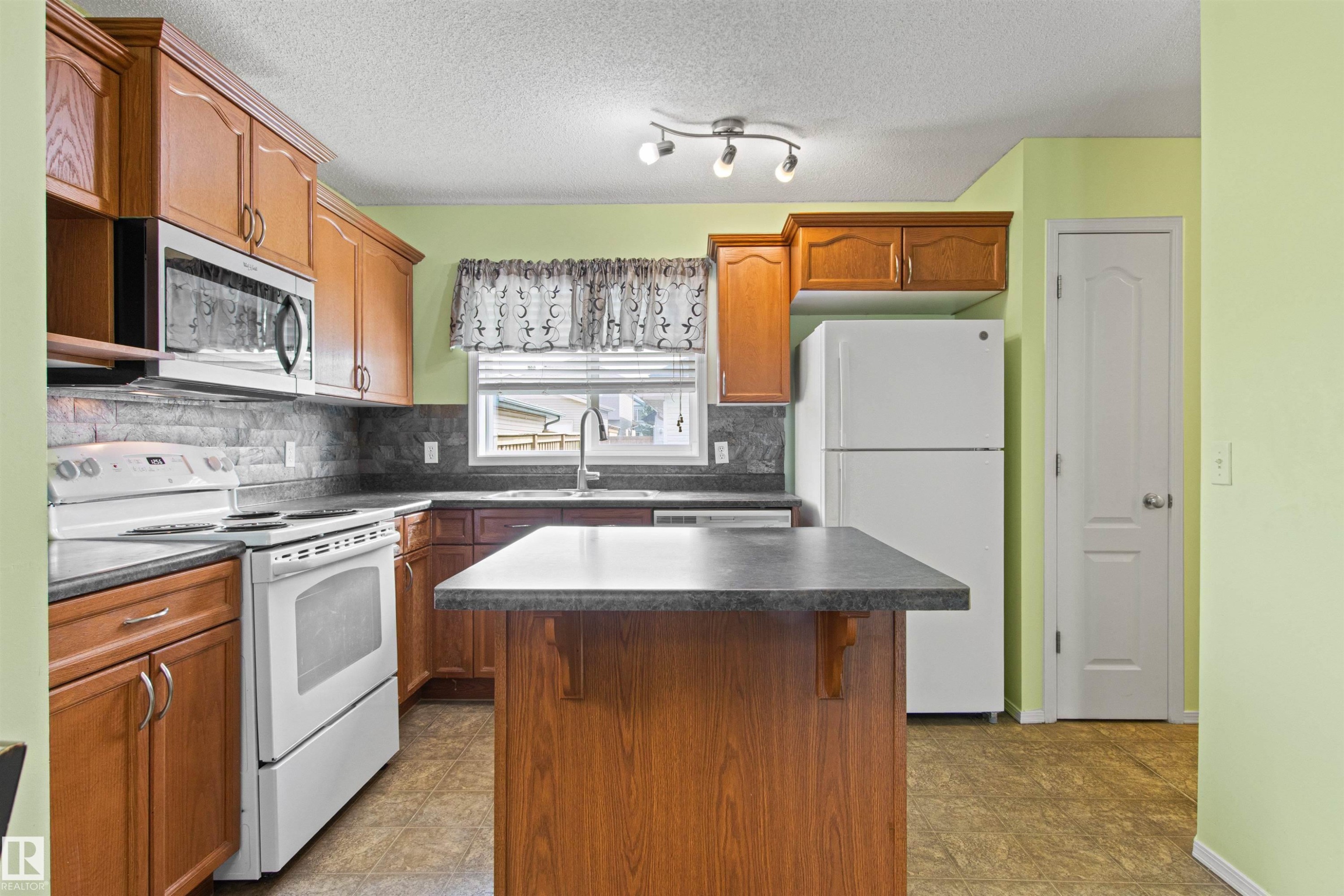 Kitchen featuring wood-finish cabinetry, a built-in microwave, a tile backsplash, and a central island with countertop - 9118 Scott Crescent Nw, Edmonton, AB - Indoor Photo Showing Kitchen