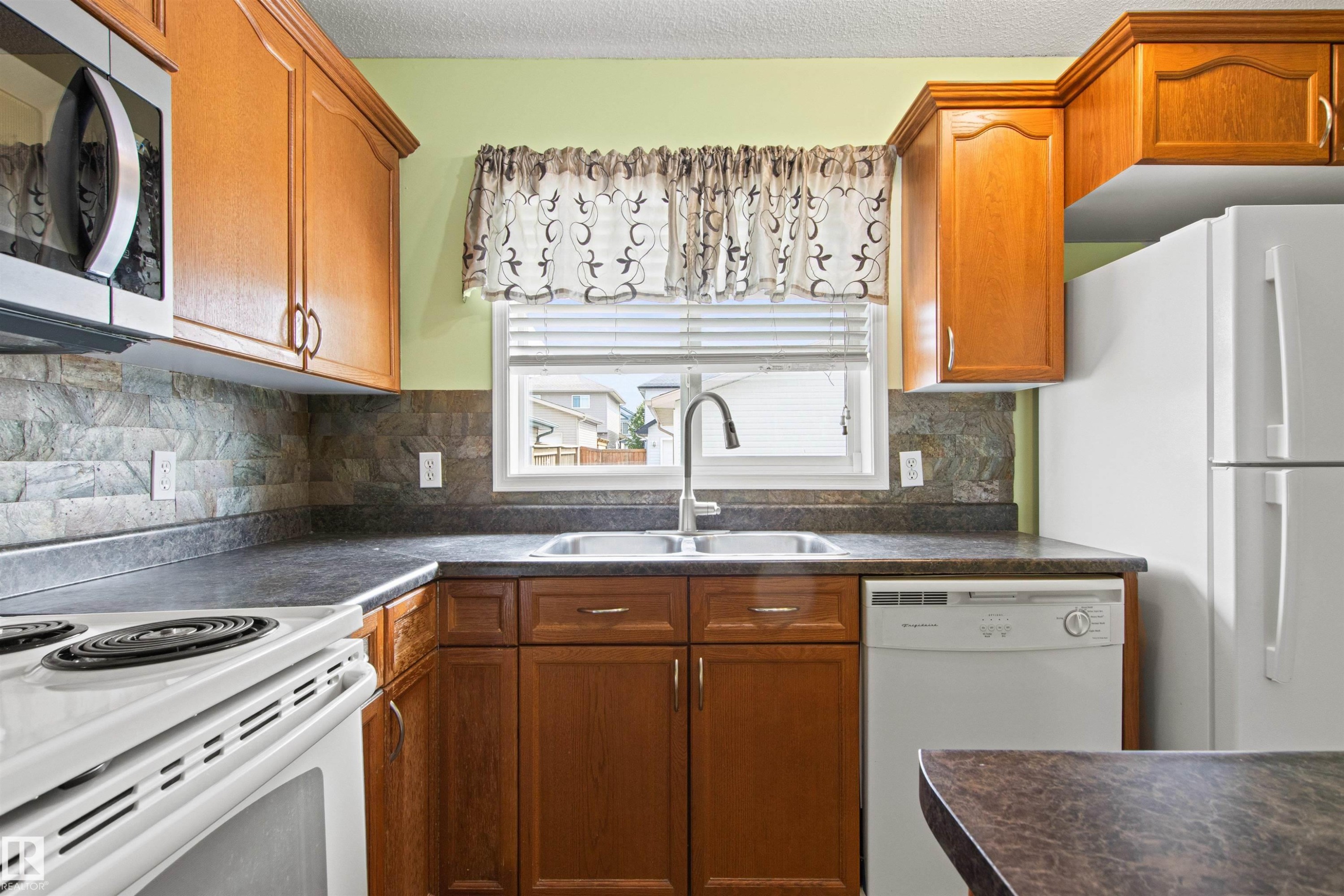 Kitchen featuring wood-finish cabinetry, dark countertops, and a tile backsplash - 9118 Scott Crescent Nw, Edmonton, AB - Indoor Photo Showing Kitchen With Double Sink