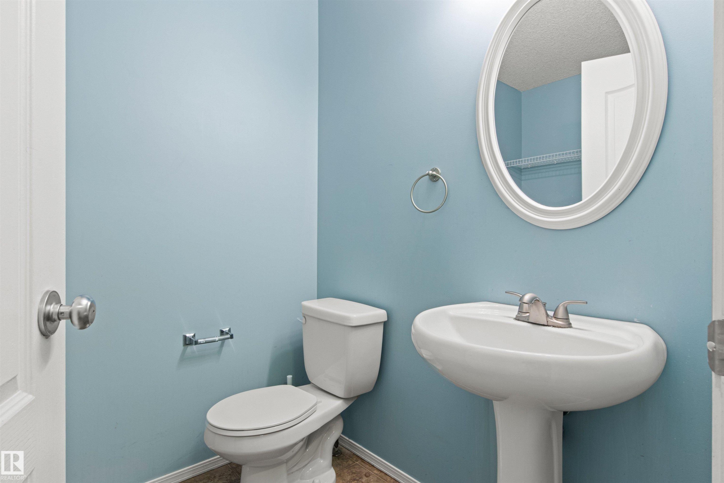 Pedestal sink with a brushed nickel faucet, oval framed mirror, and toilet - 9118 Scott Crescent Nw, Edmonton, AB - Indoor Photo Showing Bathroom