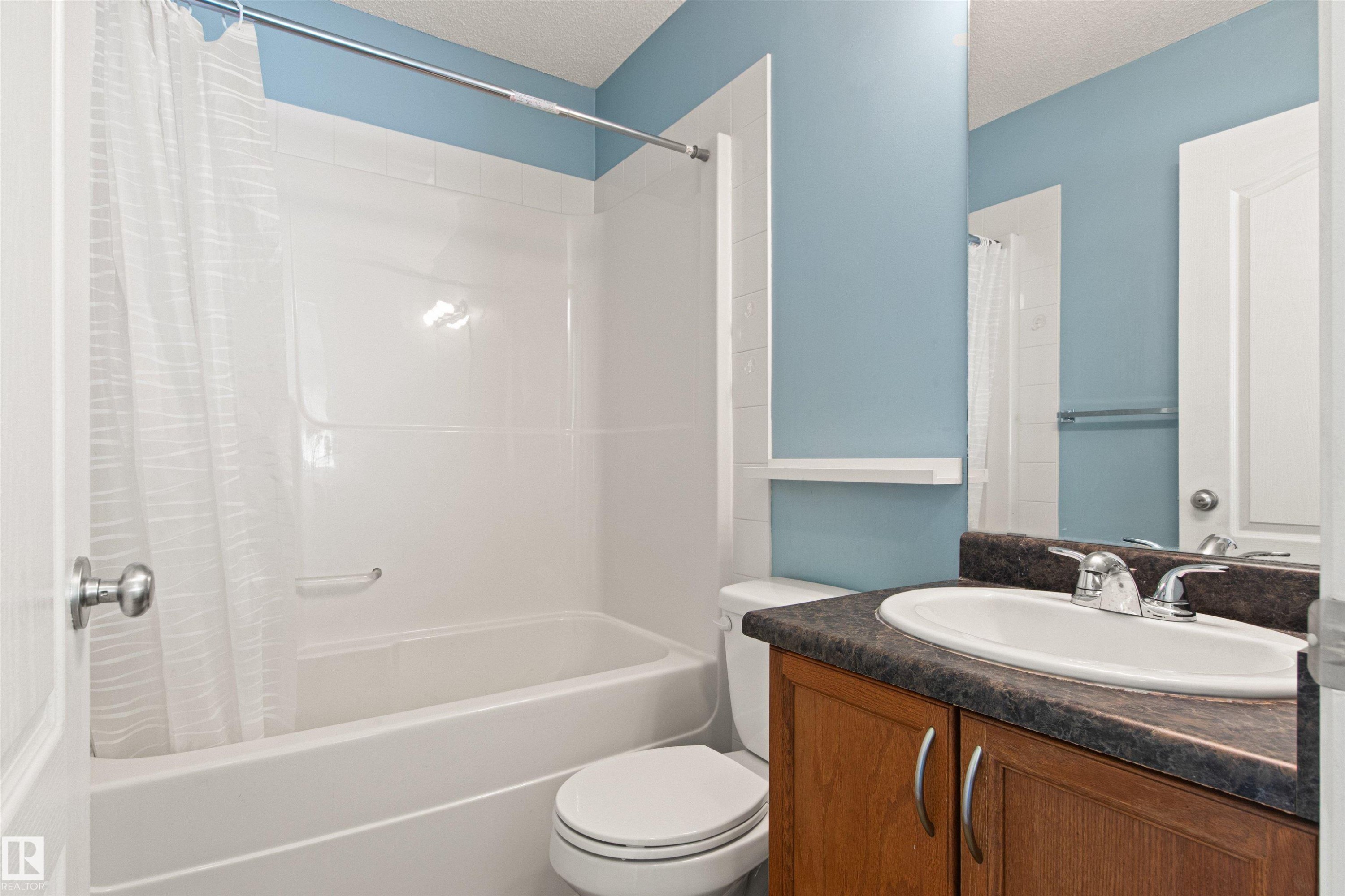 Built-in bathtub with integrated shower, white paneled surround, wood-finish vanity with a dark countertop, and an oval undermount sink with chrome fixtures - 9118 Scott Crescent Nw, Edmonton, AB - Indoor Photo Showing Bathroom
