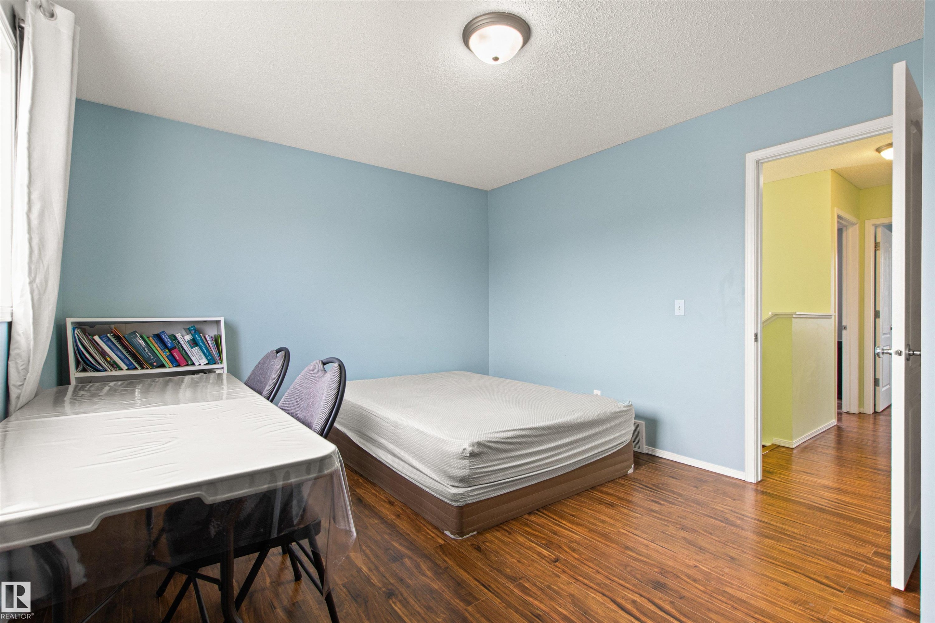 Wood-finish flooring throughout, light blue wall paint, and a ceiling-mounted light fixture - 9118 Scott Crescent Nw, Edmonton, AB - Indoor Photo Showing Bedroom