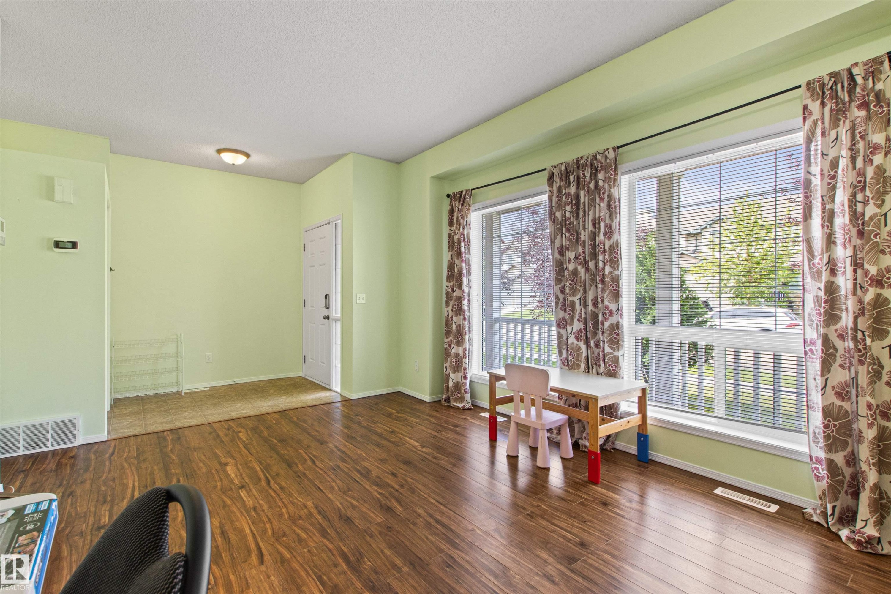 Wood-finish flooring throughout, bright window light, and a white entry door - 9118 Scott Crescent Nw, Edmonton, AB - Indoor Photo Showing Other Room