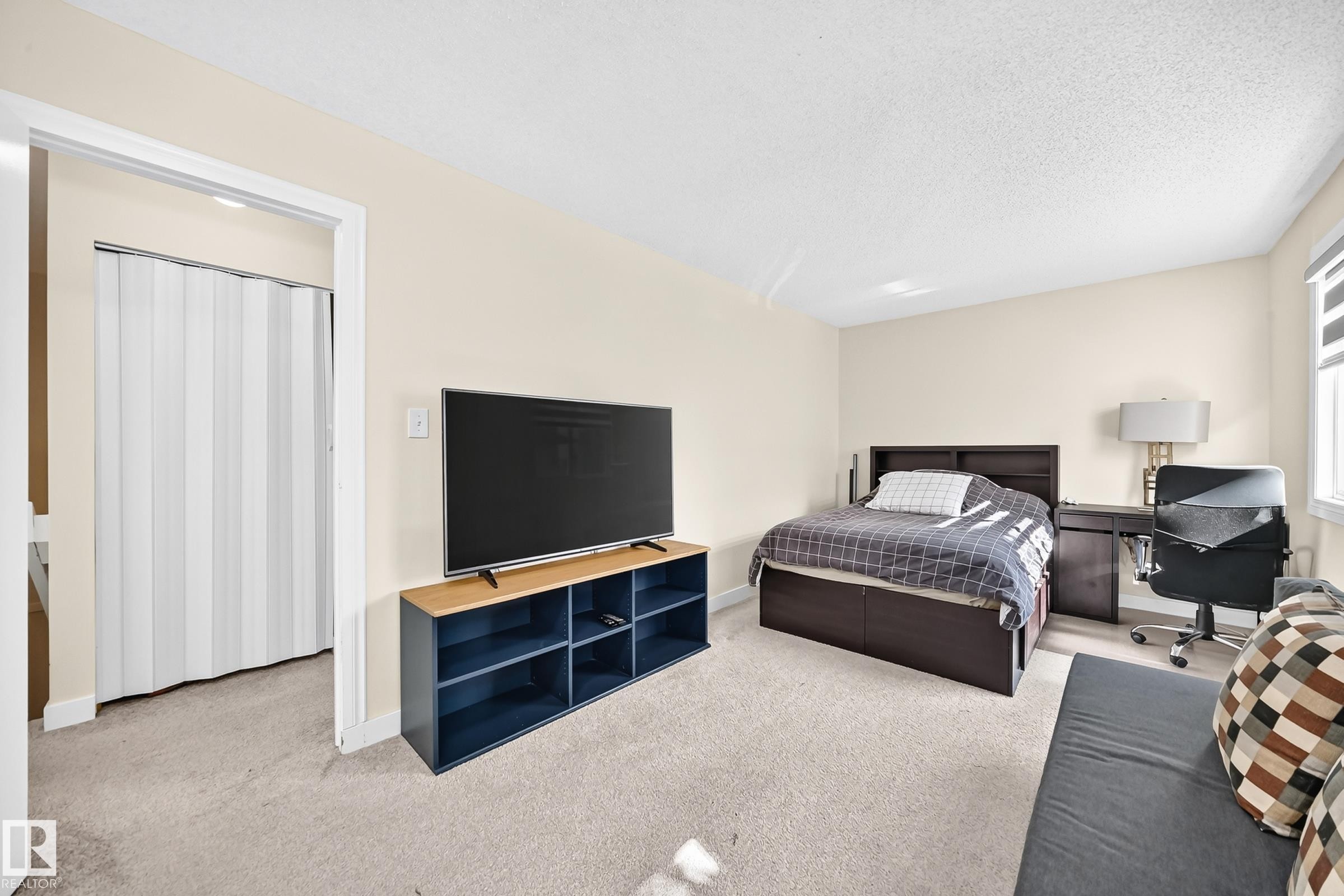 Spacious room with light-toned walls, neutral carpet flooring, and a window with roller shades - #22 3812 20 Av Nw, Edmonton, AB - Indoor Photo Showing Bedroom