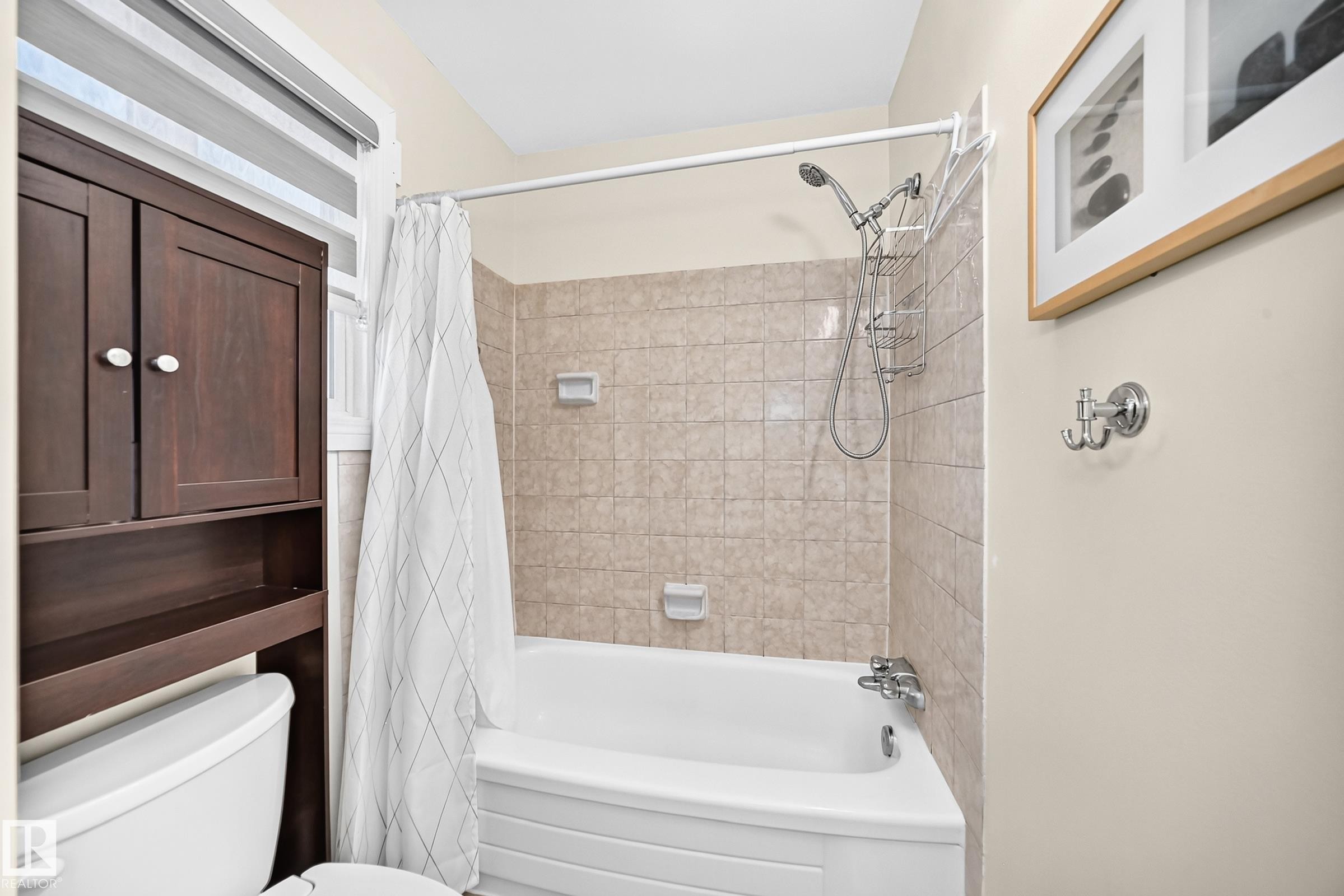 White bathtub with tiled surround, showerhead with handheld attachment, and an over-toilet storage cabinet - #22 3812 20 Av Nw, Edmonton, AB - Indoor Photo Showing Bathroom