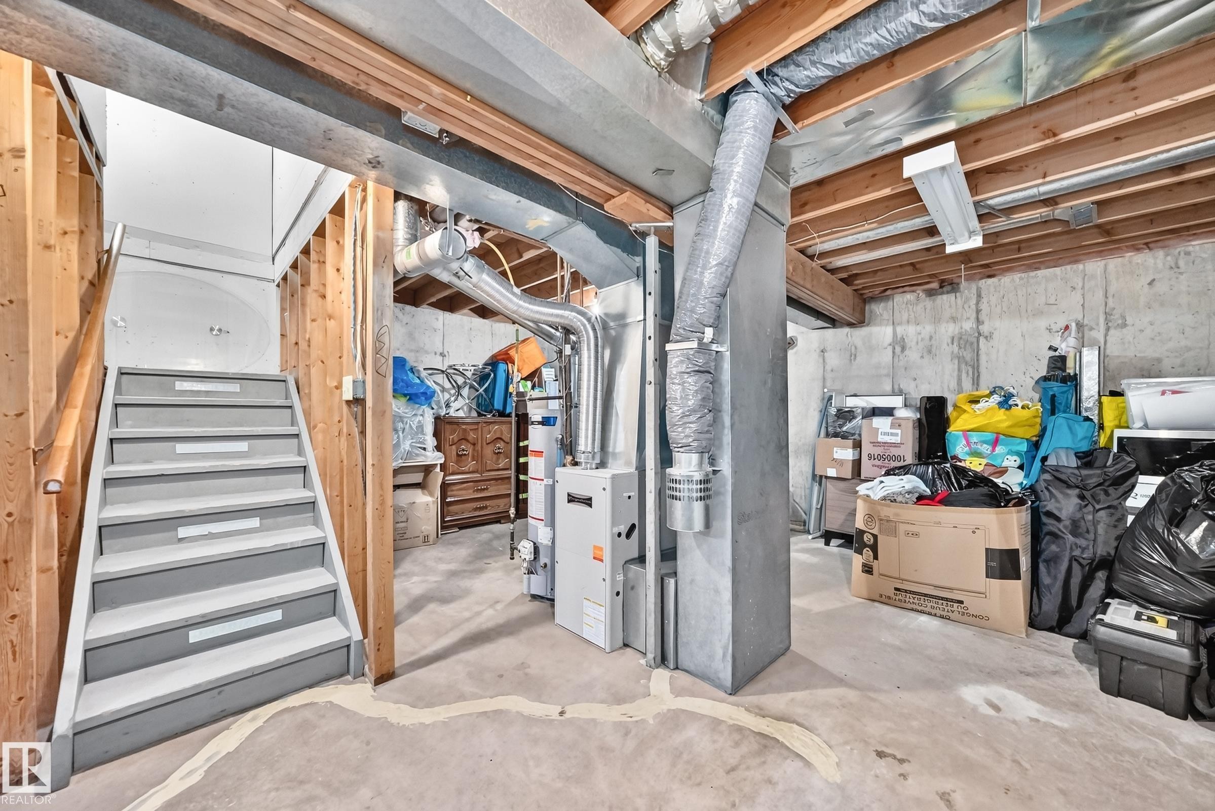 Concrete flooring, unfinished ceiling with exposed wood joists, exposed ductwork, furnace, and a water heater - #22 3812 20 Av Nw, Edmonton, AB - Indoor Photo Showing Basement