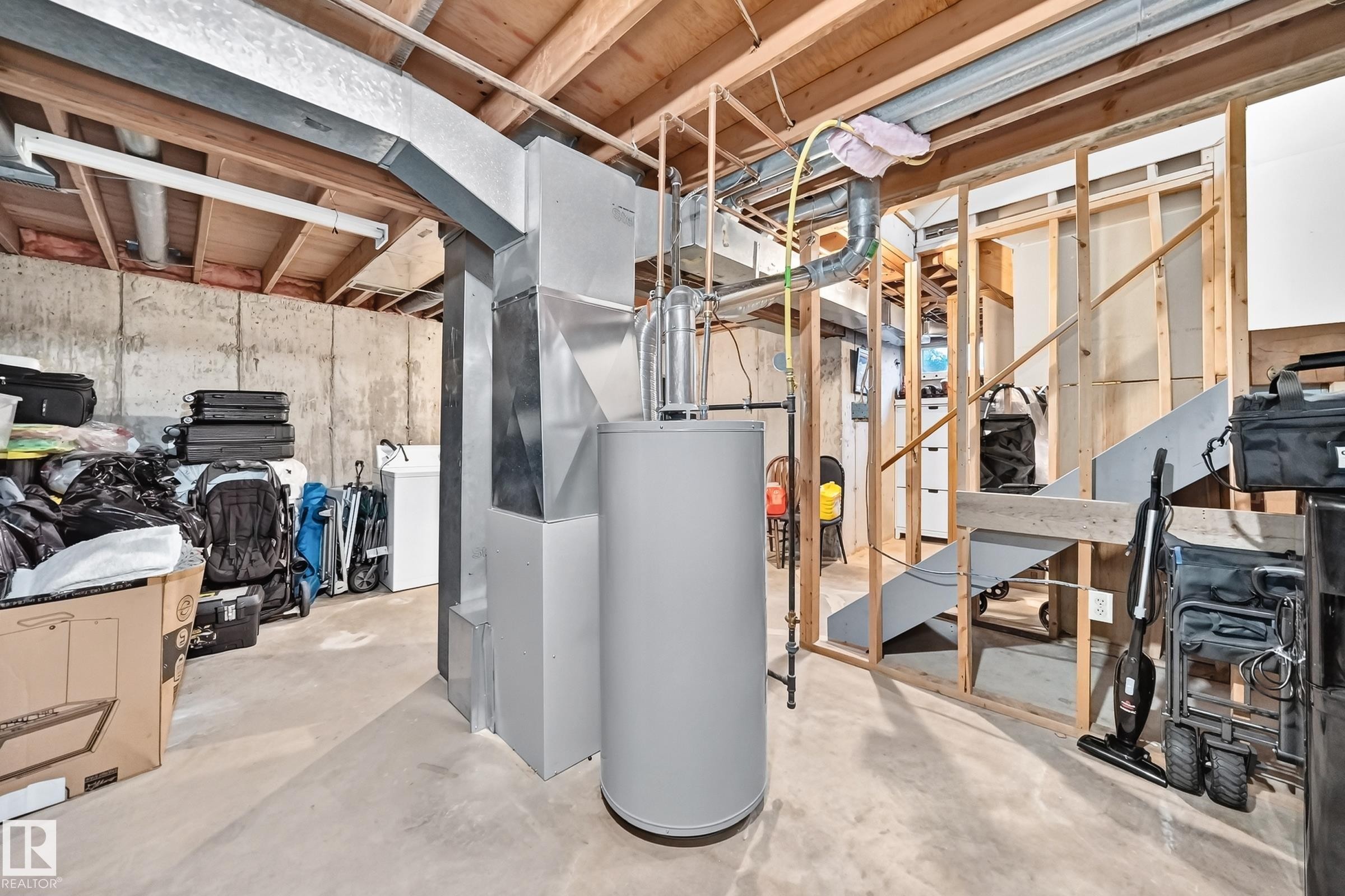 Unfinished basement featuring concrete flooring, exposed wood ceiling joists, and a water heater - #22 3812 20 Av Nw, Edmonton, AB - Indoor Photo Showing Basement