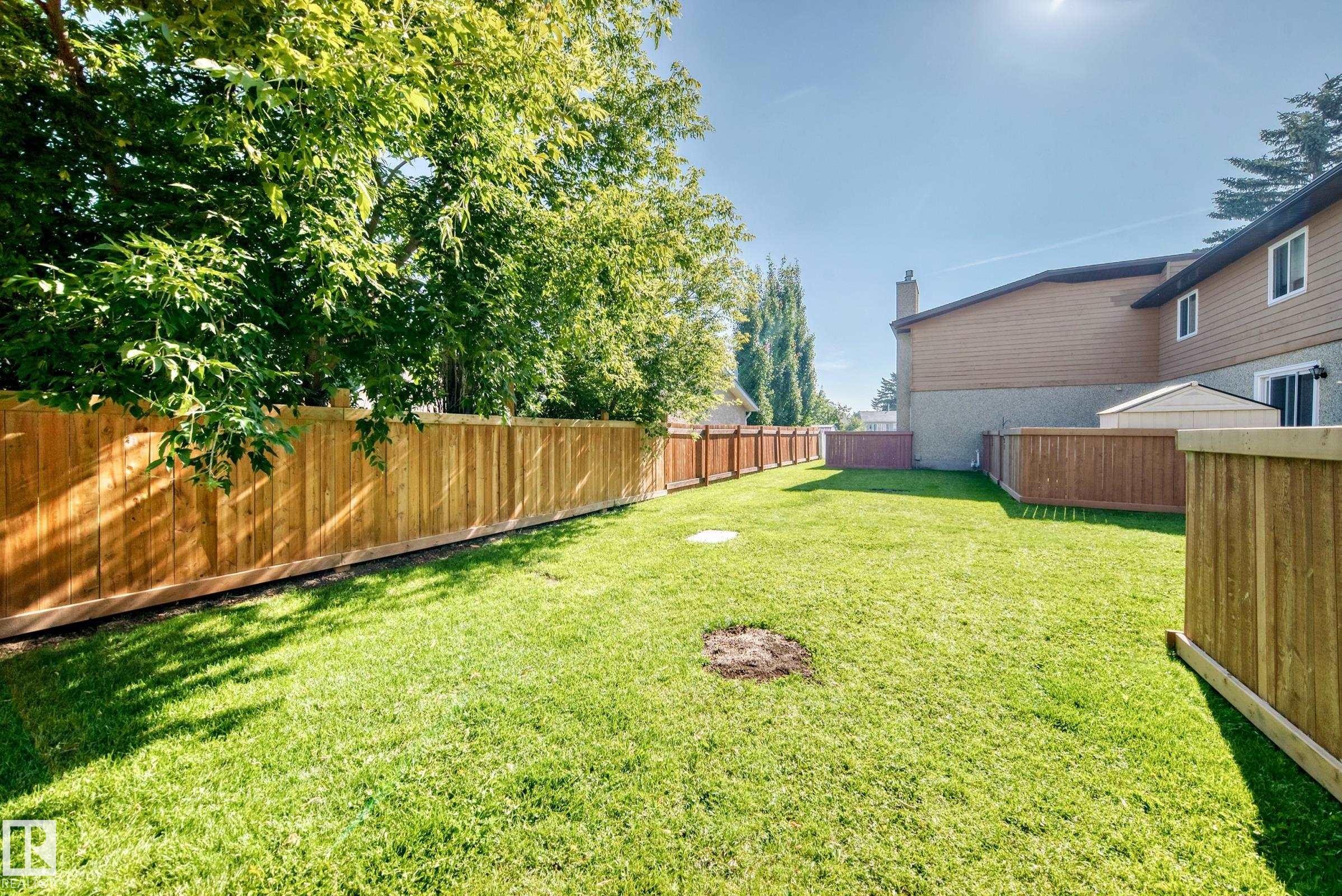 Expansive backyard featuring a manicured lawn, established perimeter trees, and a full wood-panel fence - #22 3812 20 Av Nw, Edmonton, AB - Outdoor