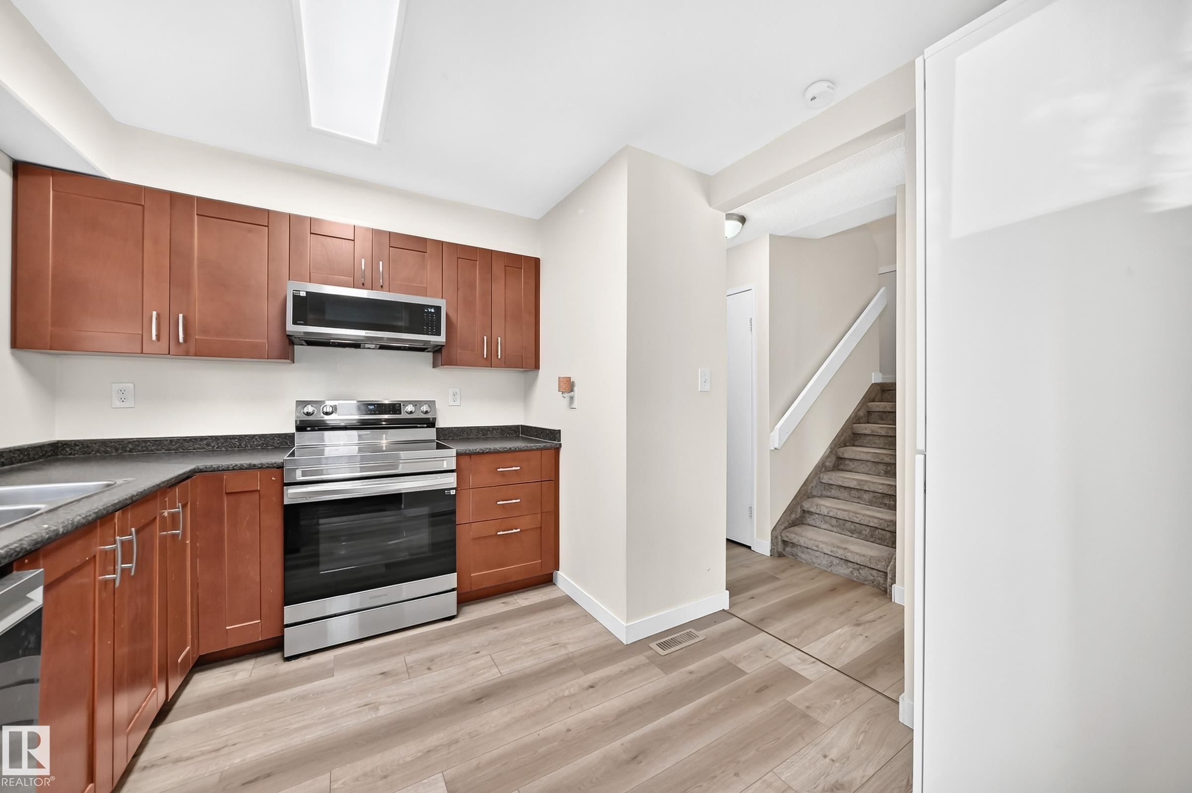 Wood-finish flooring throughout, stainless steel range, stainless steel microwave, wood cabinetry, and a carpeted staircase - #22 3812 20 Av Nw, Edmonton, AB - Indoor Photo Showing Kitchen