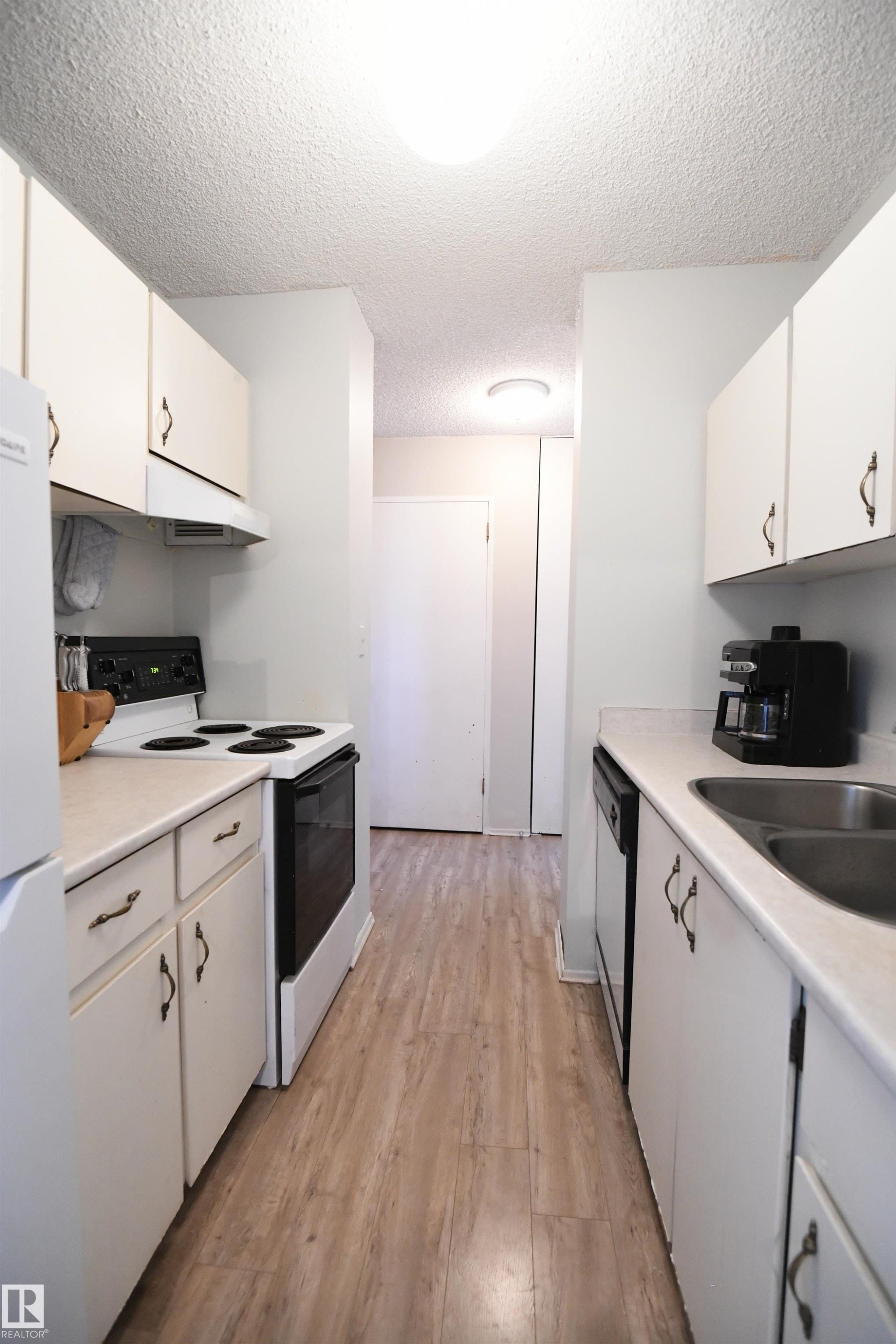 The kitchen is a simple, white, galley design, but is open at both ends, maximizing flow, and keeping the open feel - #1305 13910 Stony Plain Rd Nw, Edmonton, AB - Indoor Photo Showing Kitchen With Double Sink