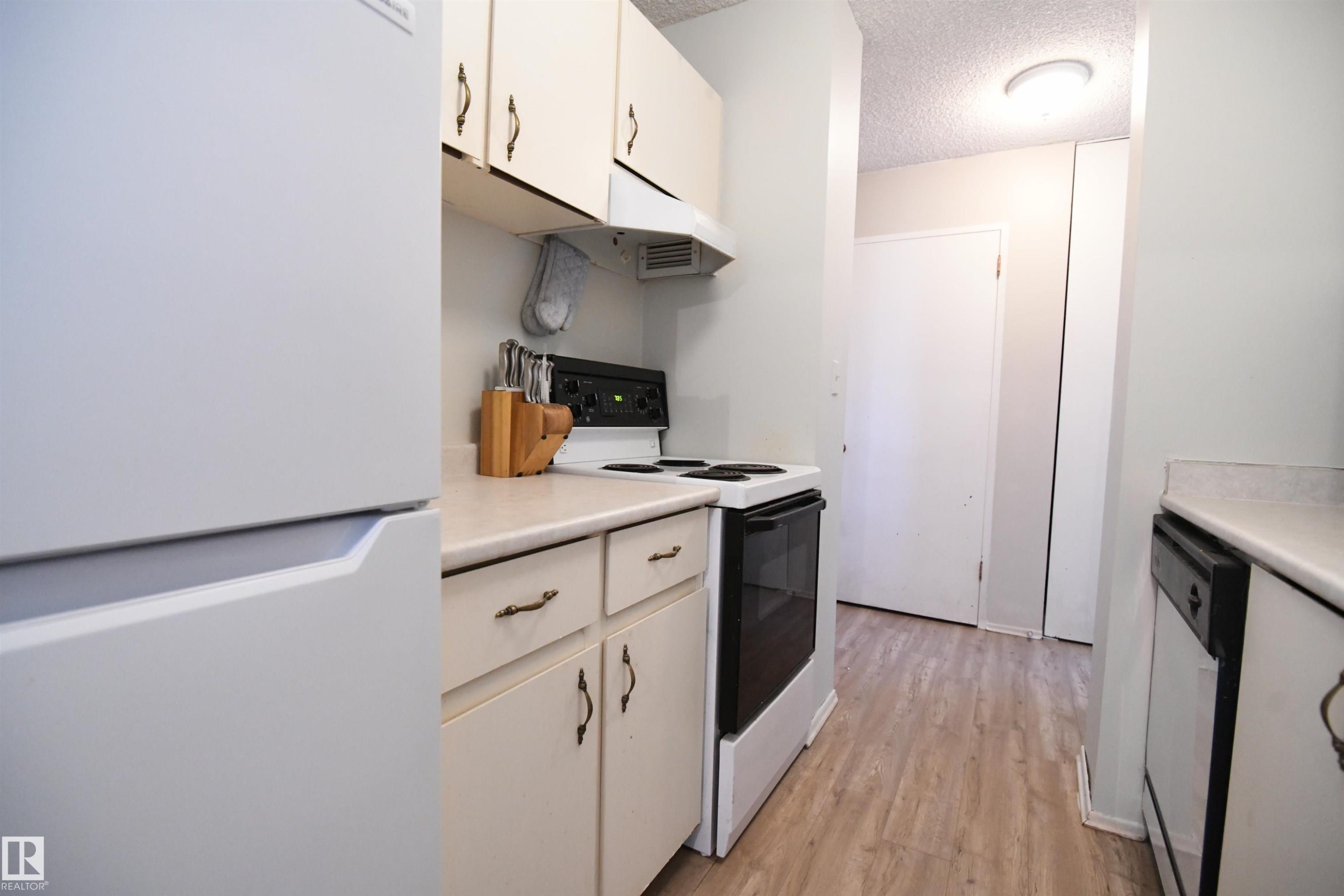 The kitchen is a simple, white, galley design, but is open at both ends, maximizing flow, and keeping the open feel - #1305 13910 Stony Plain Rd Nw, Edmonton, AB - Indoor Photo Showing Kitchen