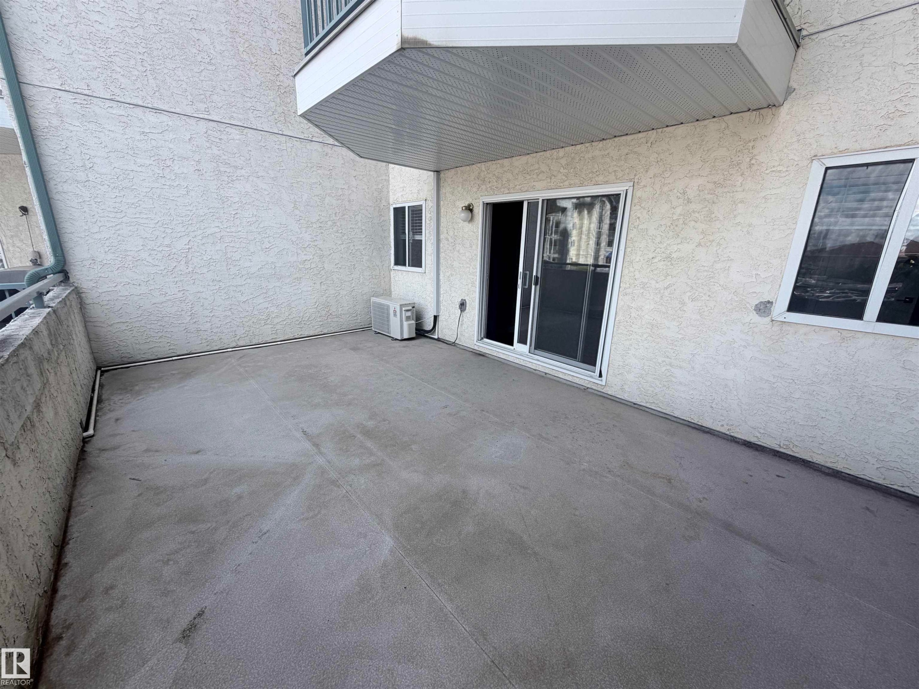 Private concrete patio with stucco exterior, a sliding glass door, and an exterior window - #208 6710 158 Av Nw, Edmonton, AB - Outdoor With Exterior