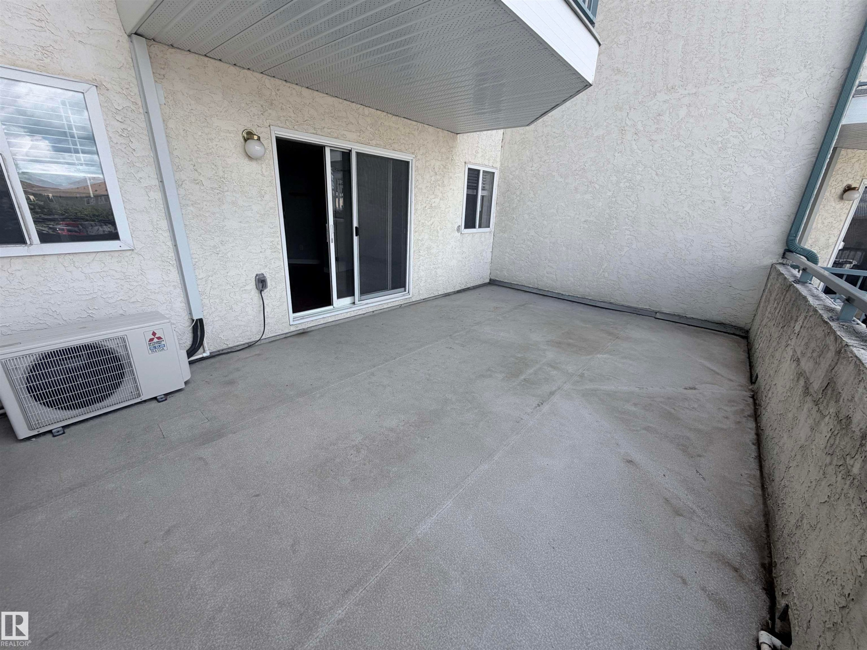 Spacious concrete patio with sliding glass door access, exterior wall sconce, and an air conditioning unit - #208 6710 158 Av Nw, Edmonton, AB - Outdoor With Exterior