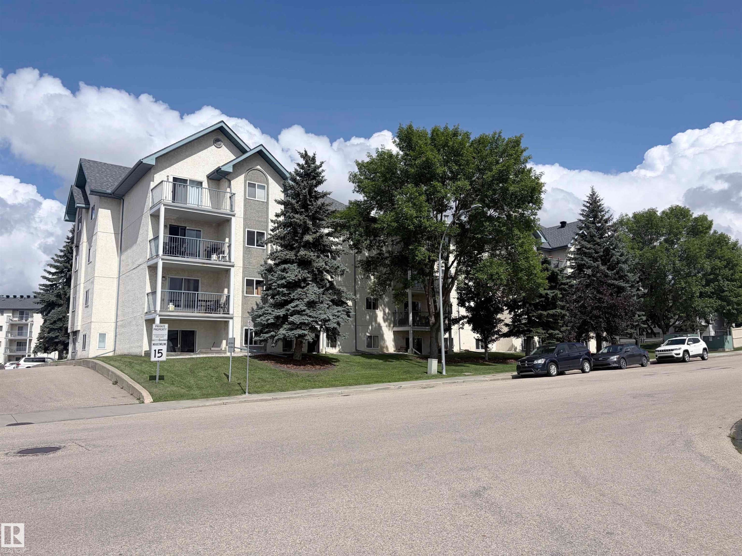 Multi-level building with individual balconies, gabled rooflines, and mature evergreen landscaping - #208 6710 158 Av Nw, Edmonton, AB - Outdoor With Balcony With Facade