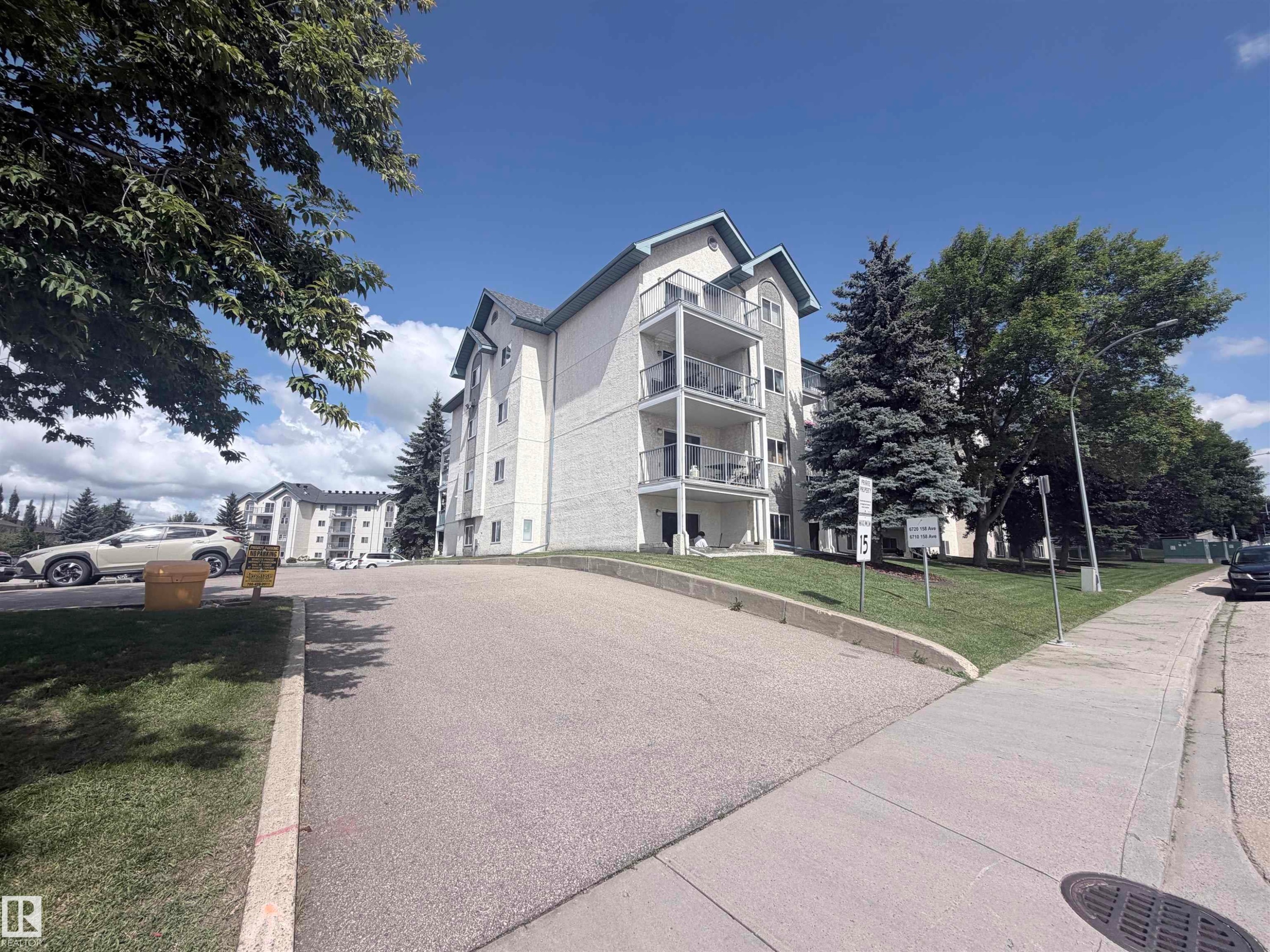 Multi-story building featuring multiple balconies, sloped roofs, and an asphalt driveway - #208 6710 158 Av Nw, Edmonton, AB - Outdoor With Balcony
