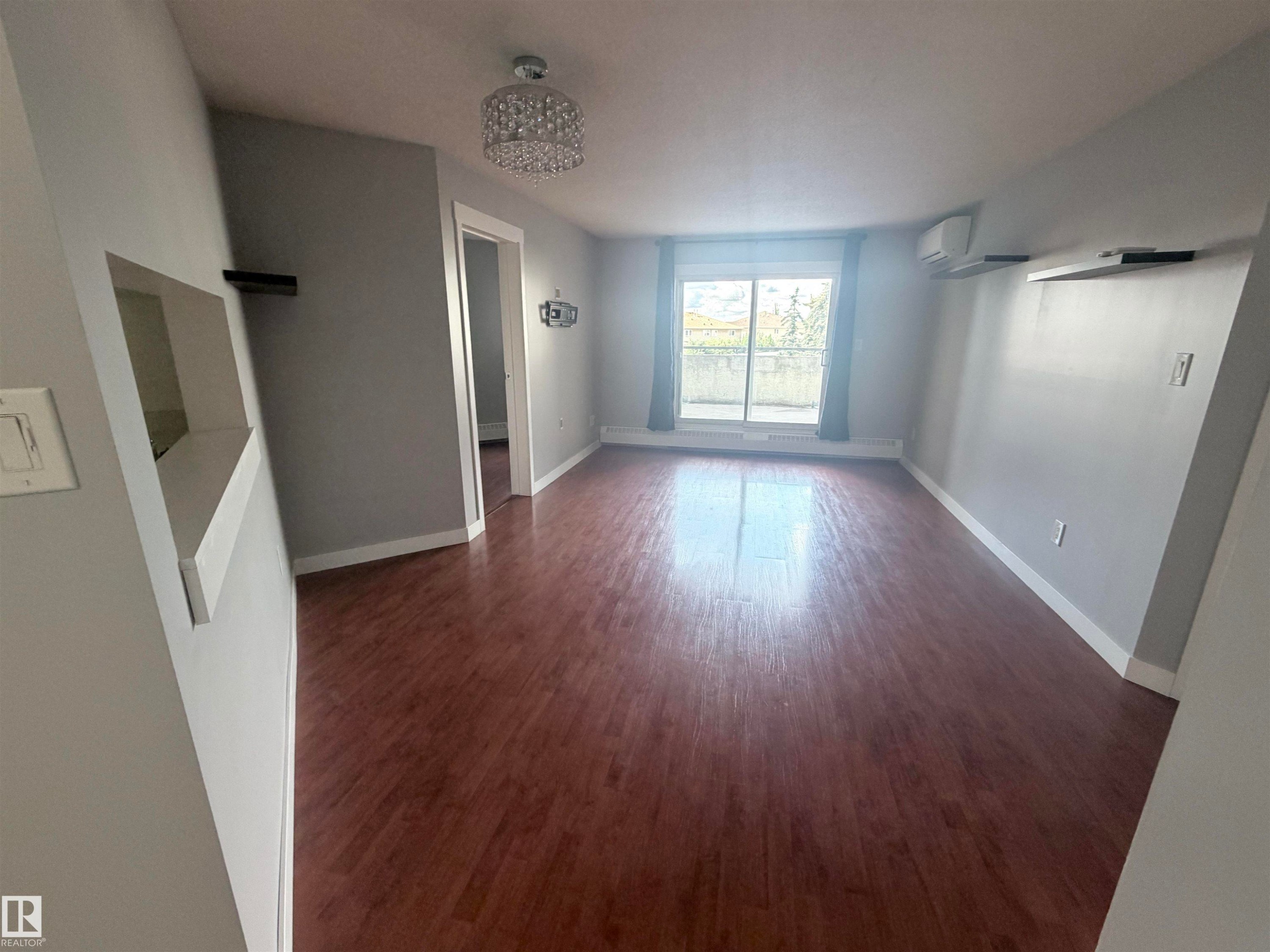 Wood-finish flooring throughout, light gray wall paint, and a decorative ceiling light fixture - #208 6710 158 Av Nw, Edmonton, AB - Indoor Photo Showing Other Room