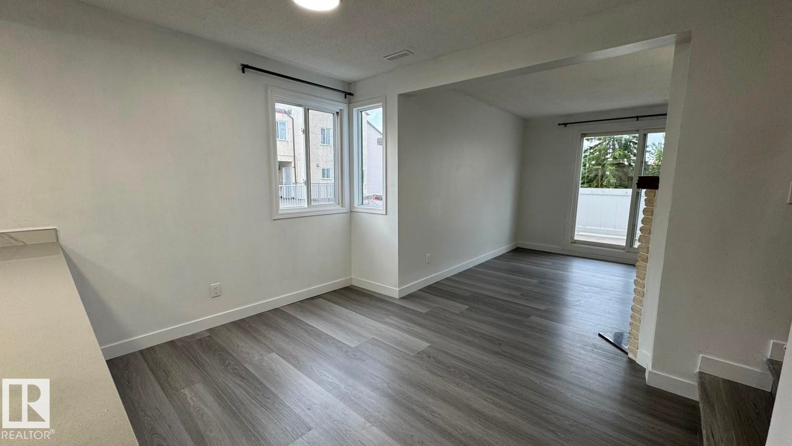 Expansive room featuring wood-finish flooring, white walls, and a large window with a black curtain rod - 41 Lancaster Terrace Nw, Edmonton, AB - Indoor Photo Showing Other Room