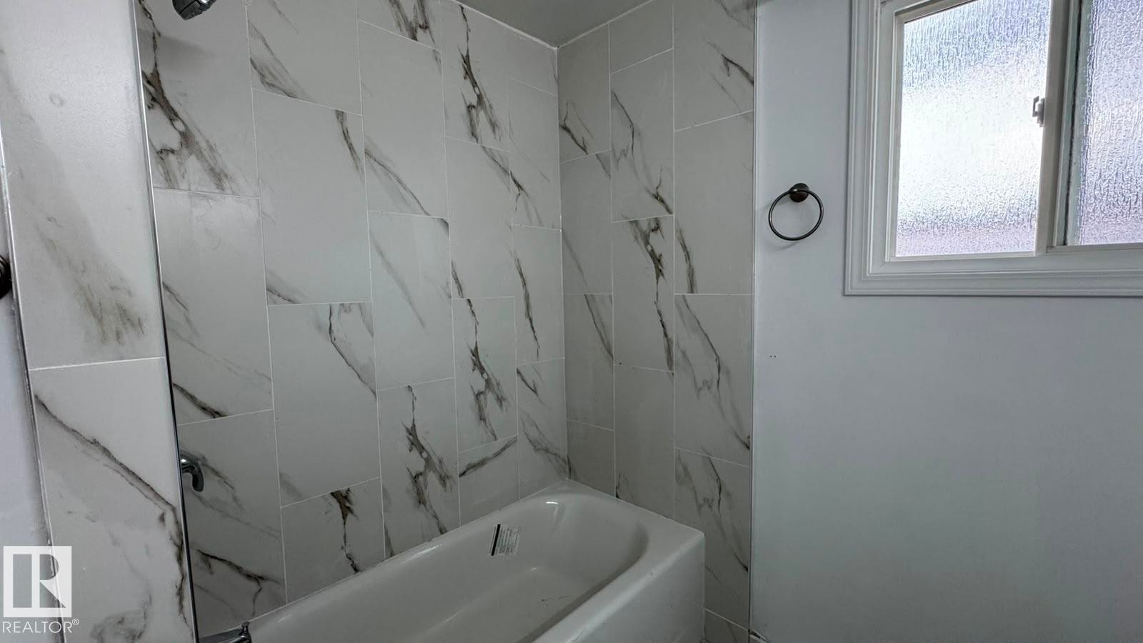 Full bathtub with a shower fixture, white tile surround with dark veining, and a frosted glass window - 41 Lancaster Terrace Nw, Edmonton, AB - Indoor Photo Showing Bathroom