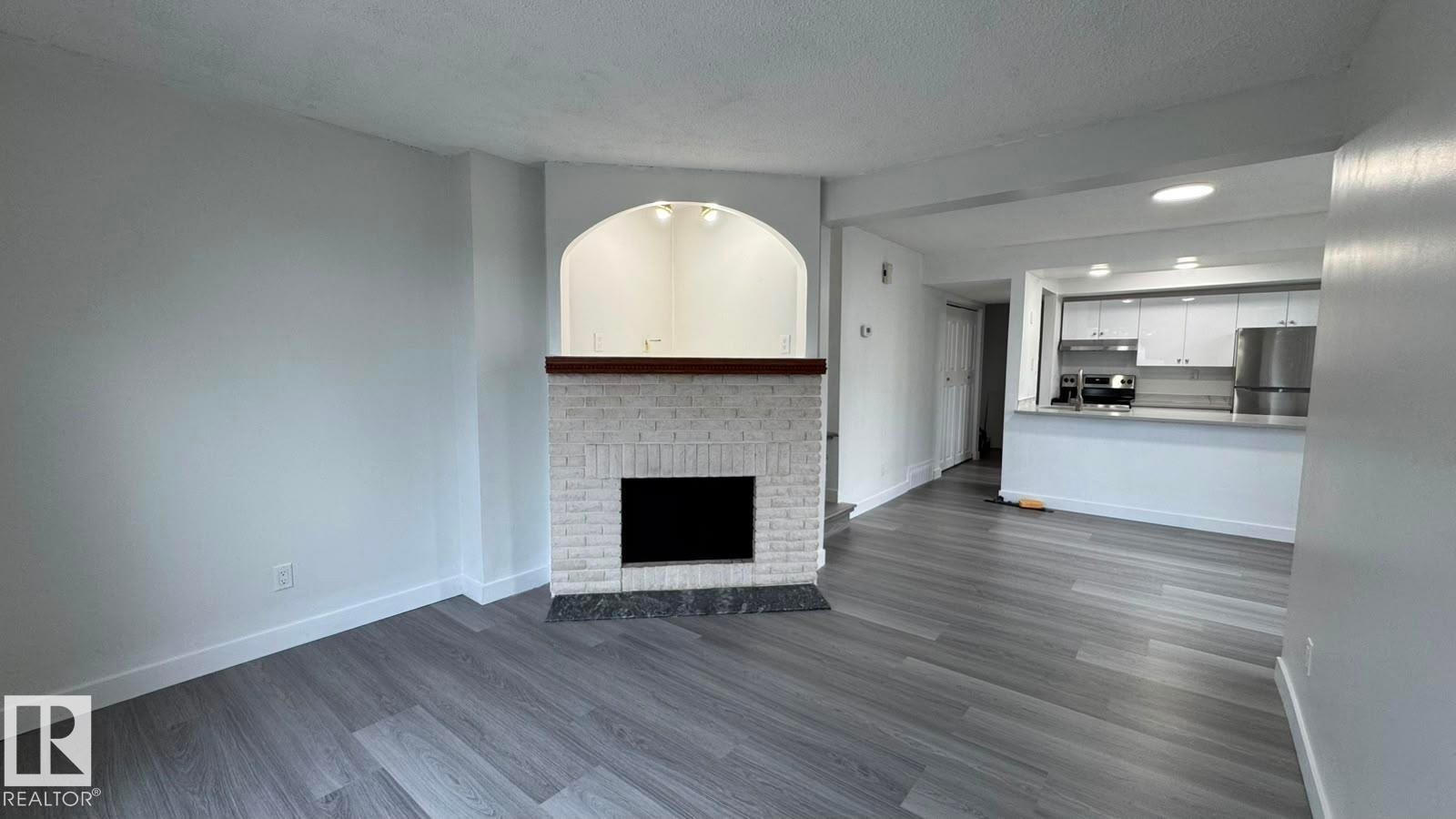 Recessed lighting, wood-finish flooring, white brick fireplace, wood mantel, stainless steel refrigerator - 41 Lancaster Terrace Nw, Edmonton, AB - Indoor Photo Showing Other Room With Fireplace