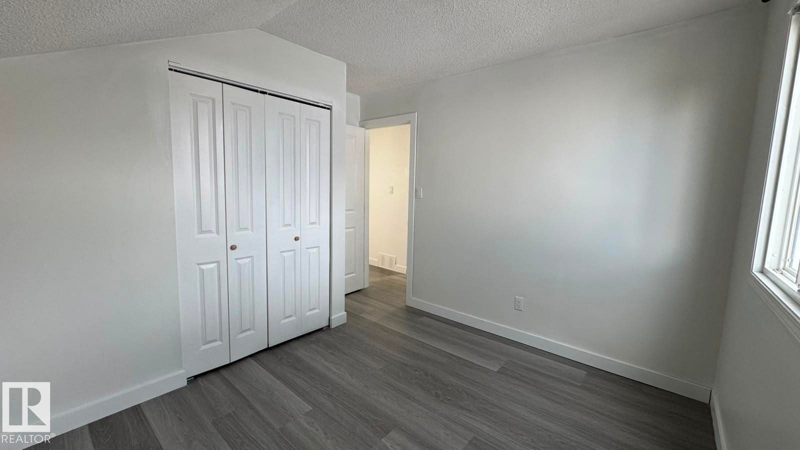 Light gray wood-finish flooring, white walls, white bi-fold closet doors with round brass hardware, white trim, and a window with blinds - 41 Lancaster Terrace Nw, Edmonton, AB - Indoor