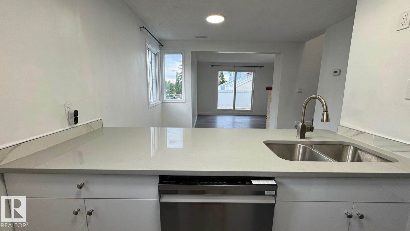 Light-toned solid surface countertop with an integrated double basin sink and gooseneck faucet, stainless steel dishwasher, and white cabinetry with brushed nickel hardware - 41 Lancaster Terrace Nw, Edmonton, AB - Indoor Photo Showing Kitchen With Double Sink