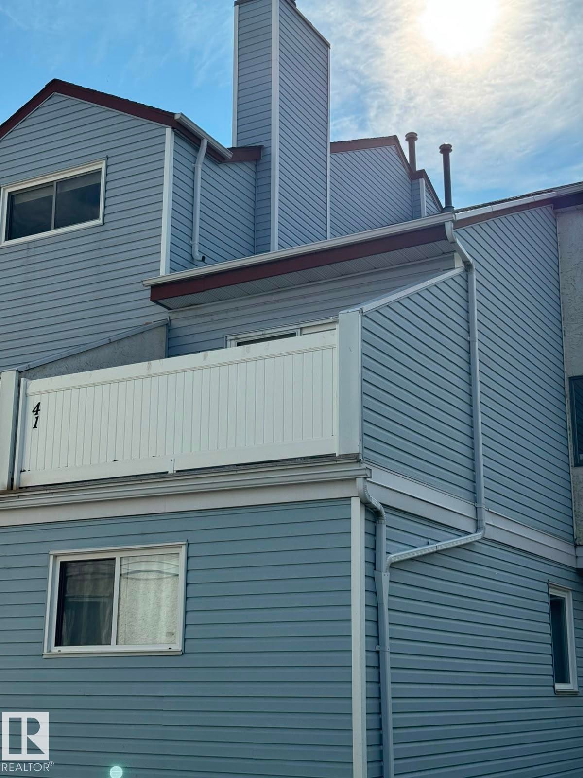 Siding exterior featuring a prominent chimney structure, multiple windows, and a white balcony railing - 41 Lancaster Terrace Nw, Edmonton, AB - Outdoor With Exterior