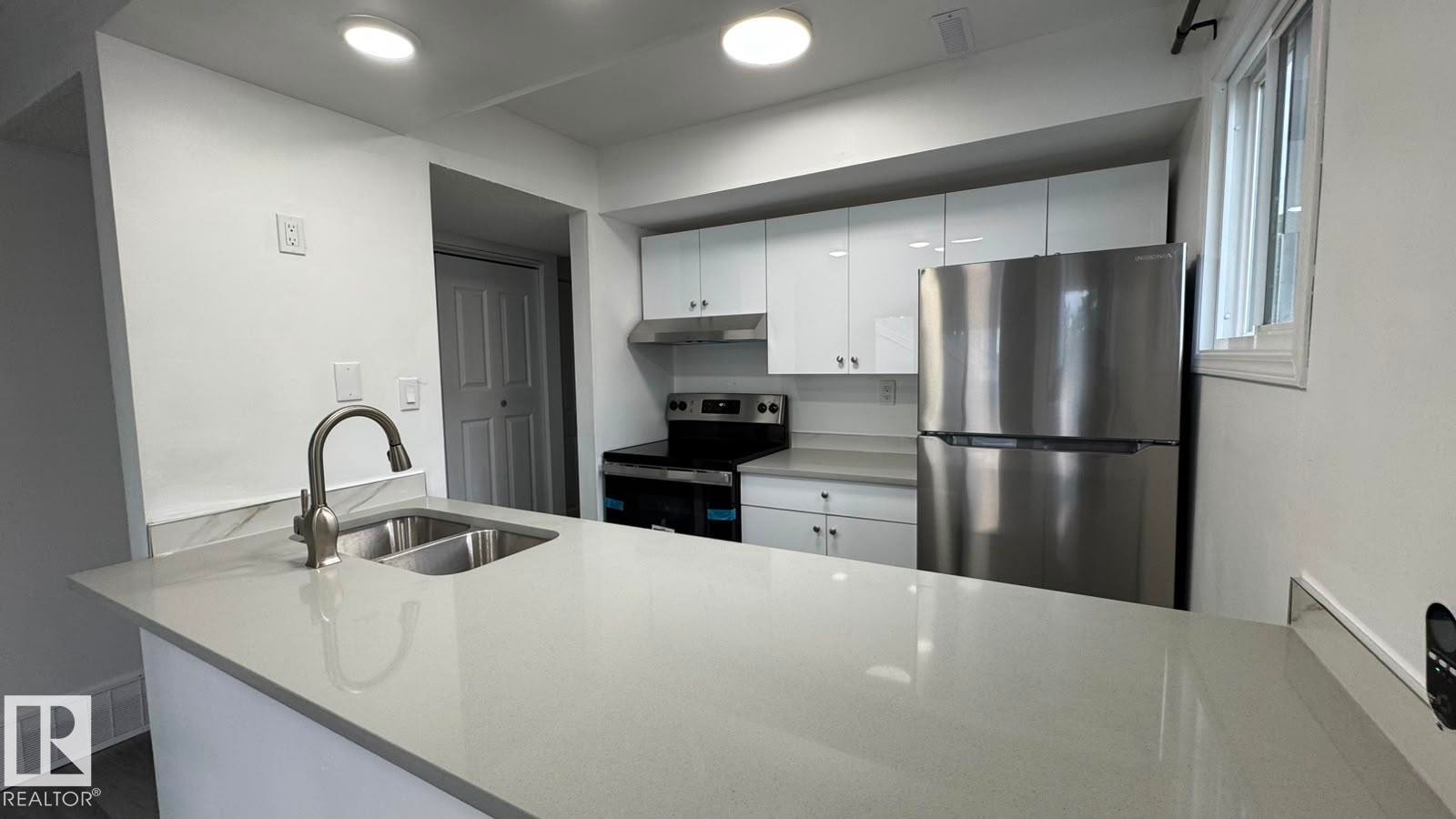 Kitchen featuring a dual basin sink with a gooseneck faucet, light-toned countertops, white cabinetry, and stainless steel appliances - 41 Lancaster Terrace Nw, Edmonton, AB - Indoor Photo Showing Kitchen With Double Sink With Upgraded Kitchen