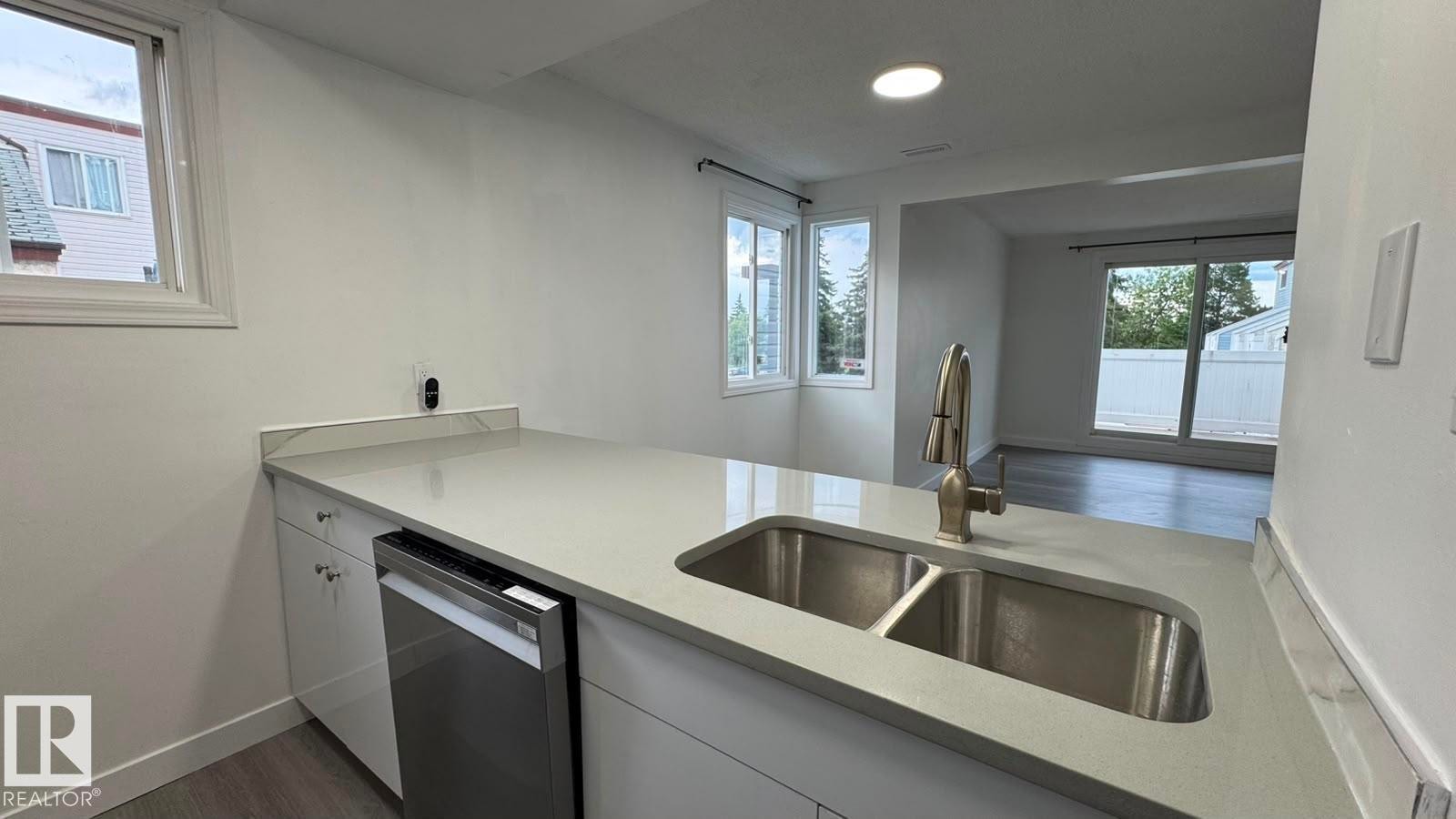 Kitchen island with light-toned countertop, stainless steel double basin sink, and a high-arc faucet - 41 Lancaster Terrace Nw, Edmonton, AB - Indoor Photo Showing Kitchen With Double Sink