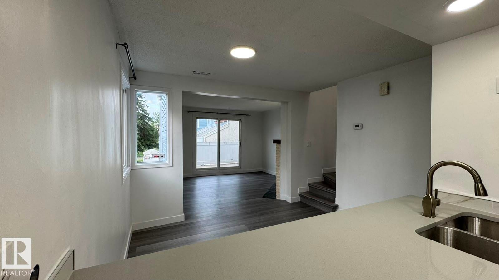 Spacious interior with wood-finish flooring, recessed lighting, and a kitchen featuring a dual-basin sink with a gooseneck faucet - 41 Lancaster Terrace Nw, Edmonton, AB - Indoor