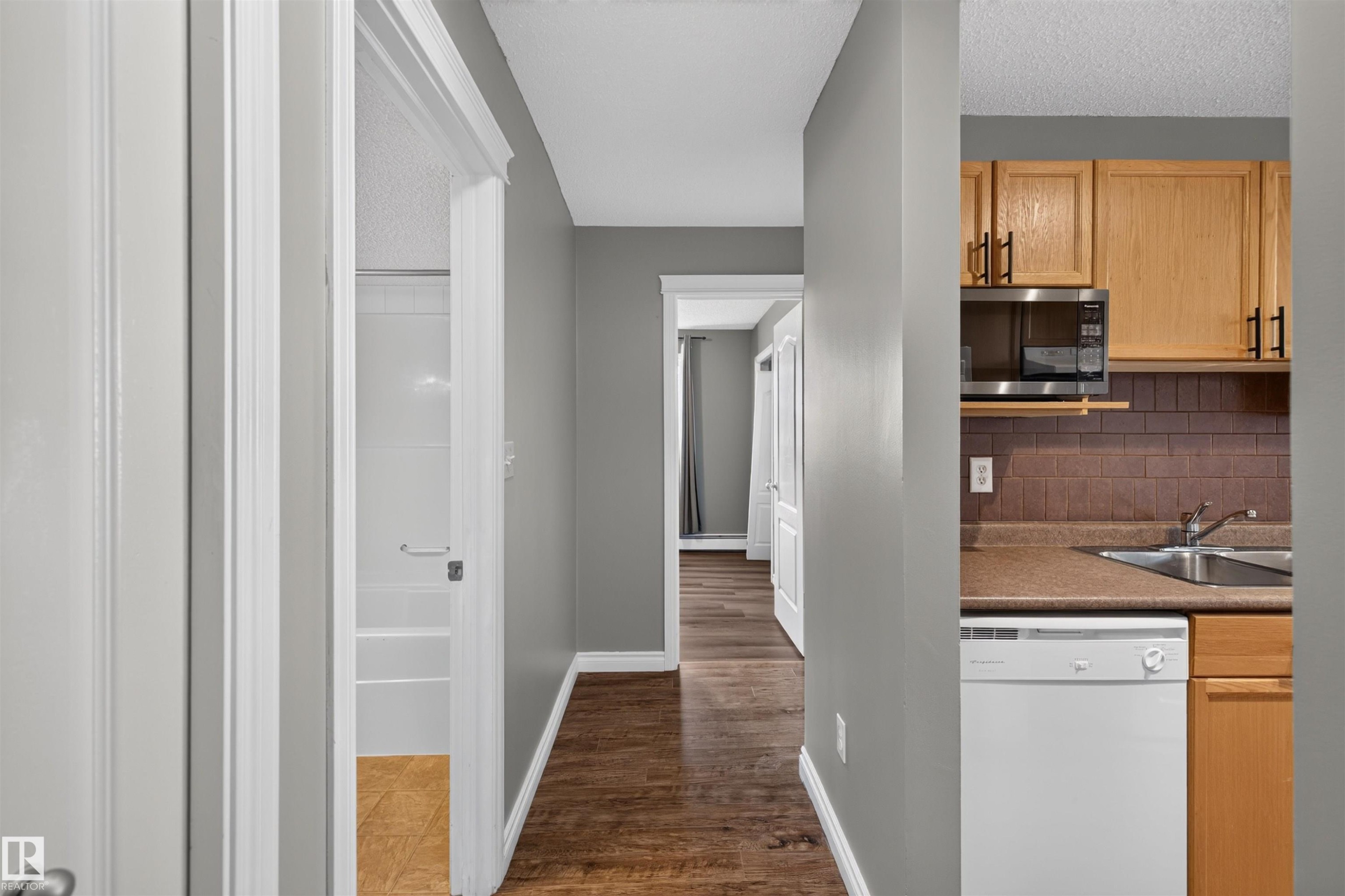 Galley kitchen featuring wood-finish cabinetry, stainless steel microwave, and dual basin sink - #4 4616 47 St, Leduc, AB - Indoor
