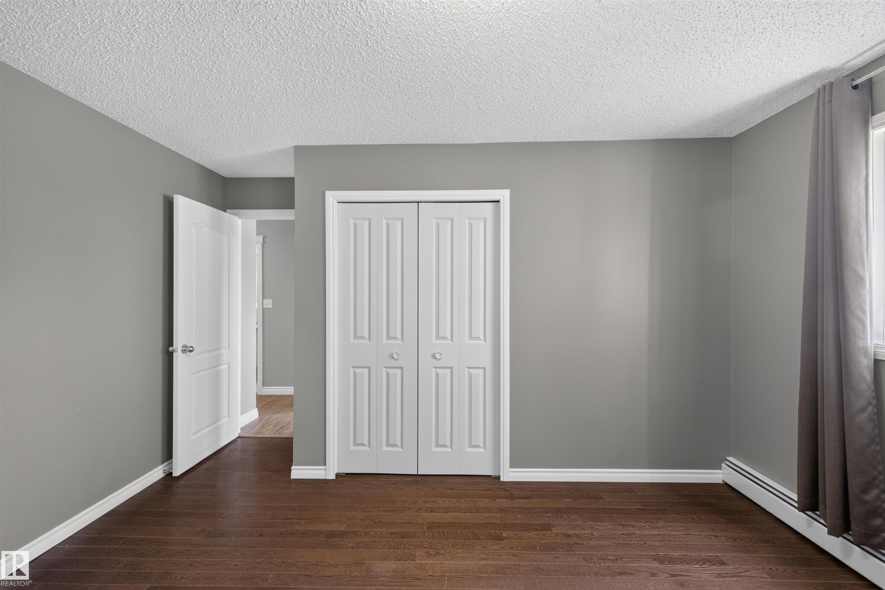 Dark wood-finish flooring with white trim, neutral gray walls, and white bi-fold closet doors - #4 4616 47 St, Leduc, AB - Indoor Photo Showing Other Room