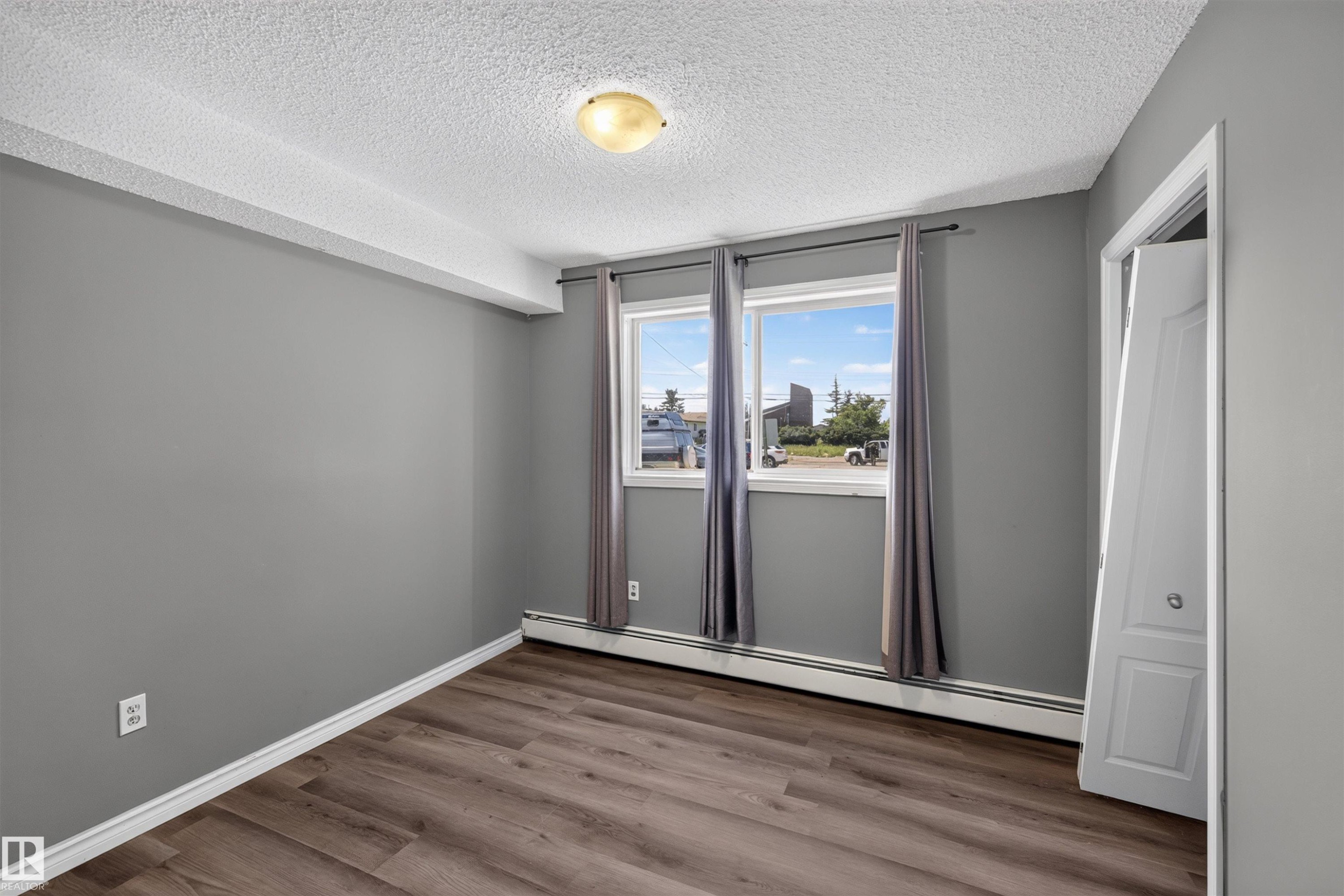 Wood-finish flooring, dual windows, ceiling-mounted light fixture, and white bi-fold closet door - #4 4616 47 St, Leduc, AB - Indoor Photo Showing Other Room