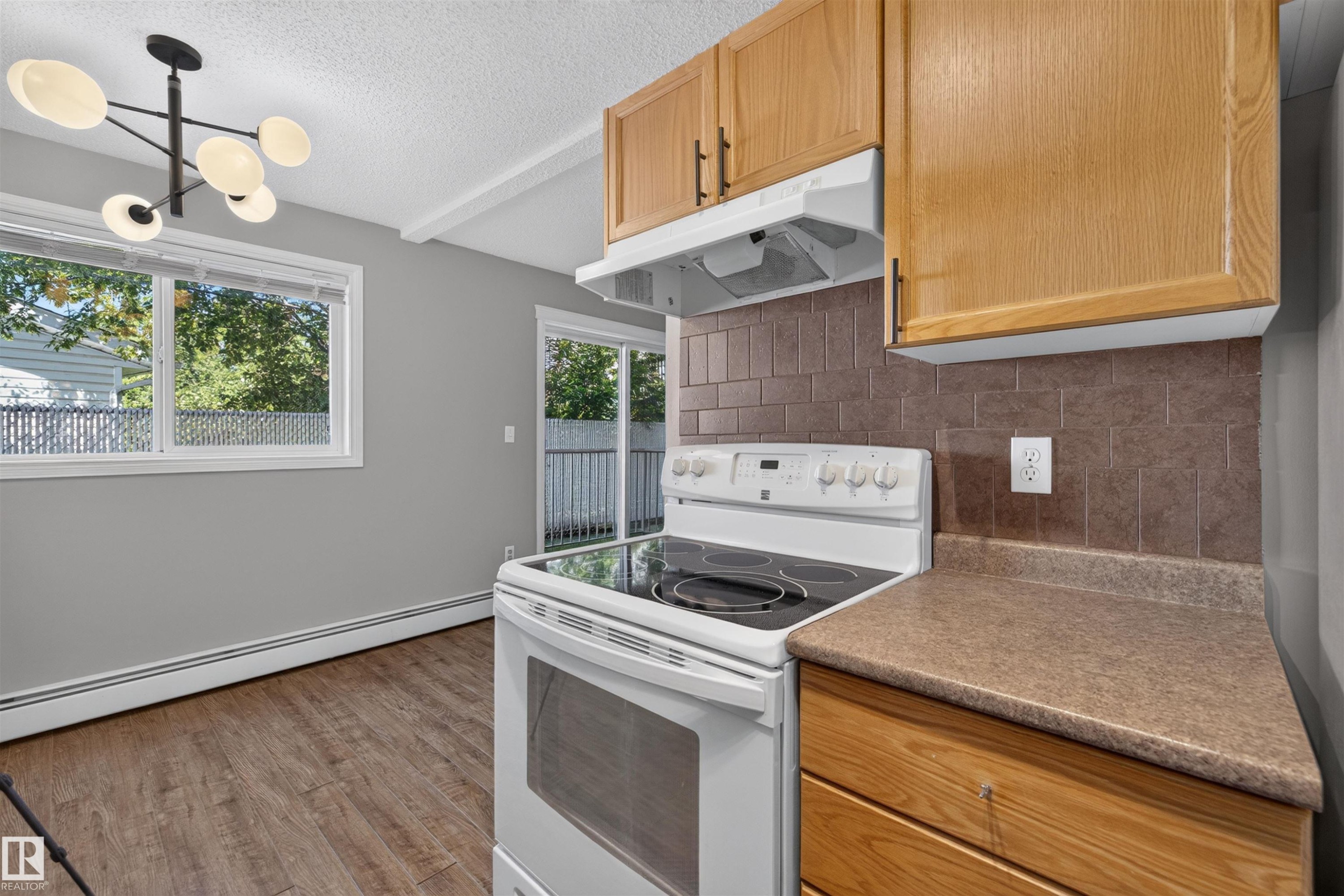 Wood-finish flooring, white window trim, contemporary ceiling light fixture, sliding glass patio door, and wood cabinetry - #4 4616 47 St, Leduc, AB - Indoor Photo Showing Kitchen