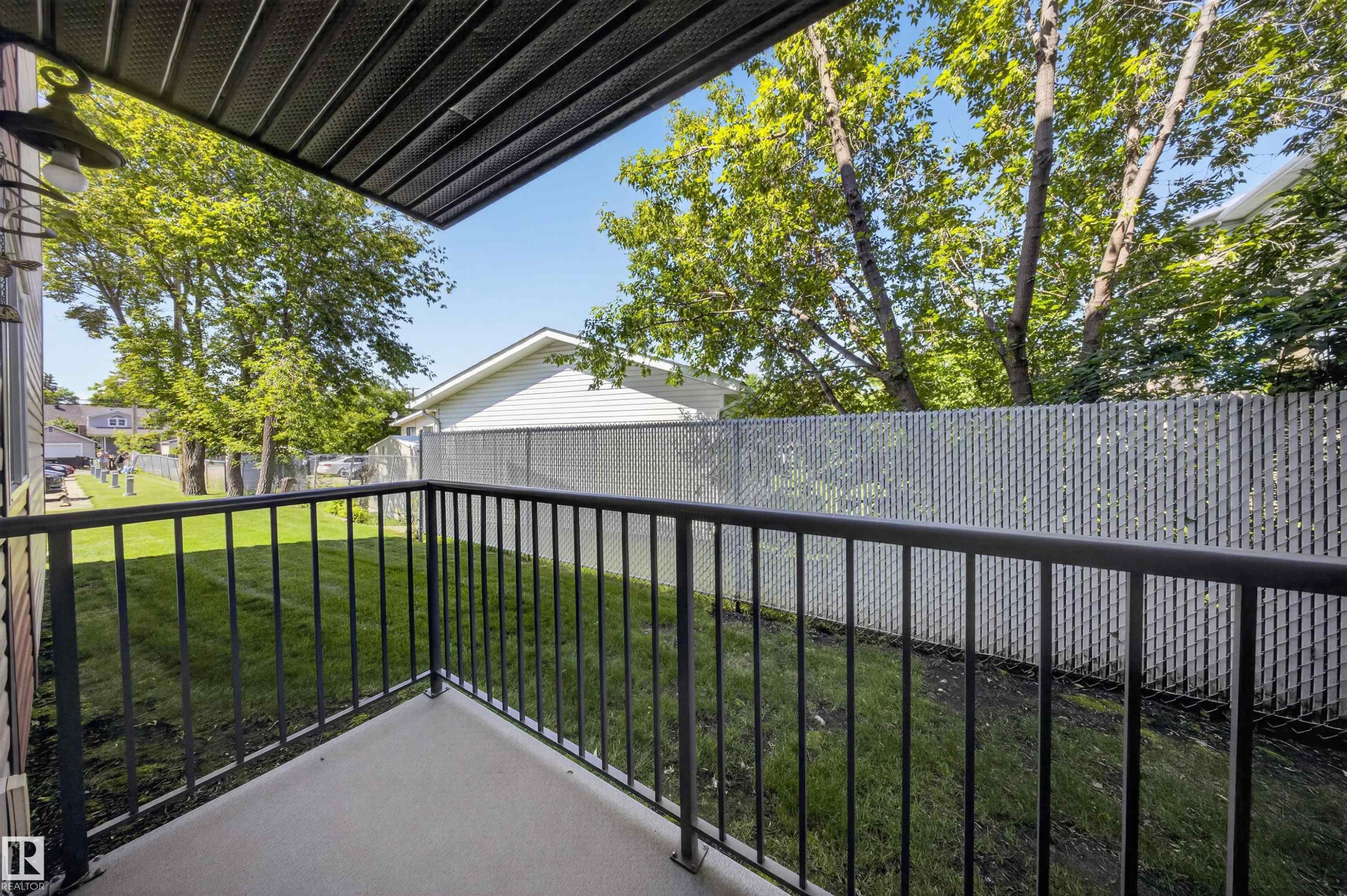 Private patio with concrete flooring and black metal railings, overlooking a fenced yard with mature trees - #4 4616 47 St, Leduc, AB - Outdoor With Exterior