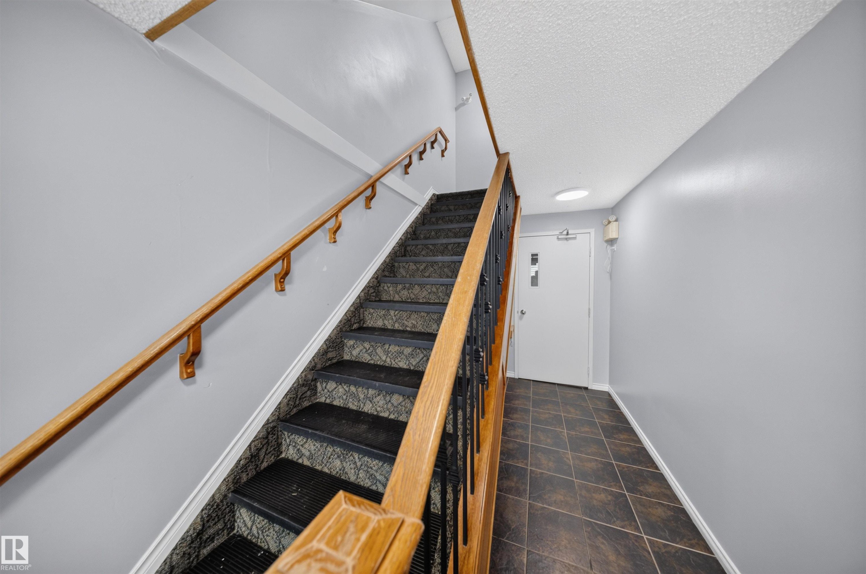 Stairwell with wood-finish handrails, patterned stair runners, and tiled flooring - #4 4616 47 St, Leduc, AB - Indoor Photo Showing Other Room