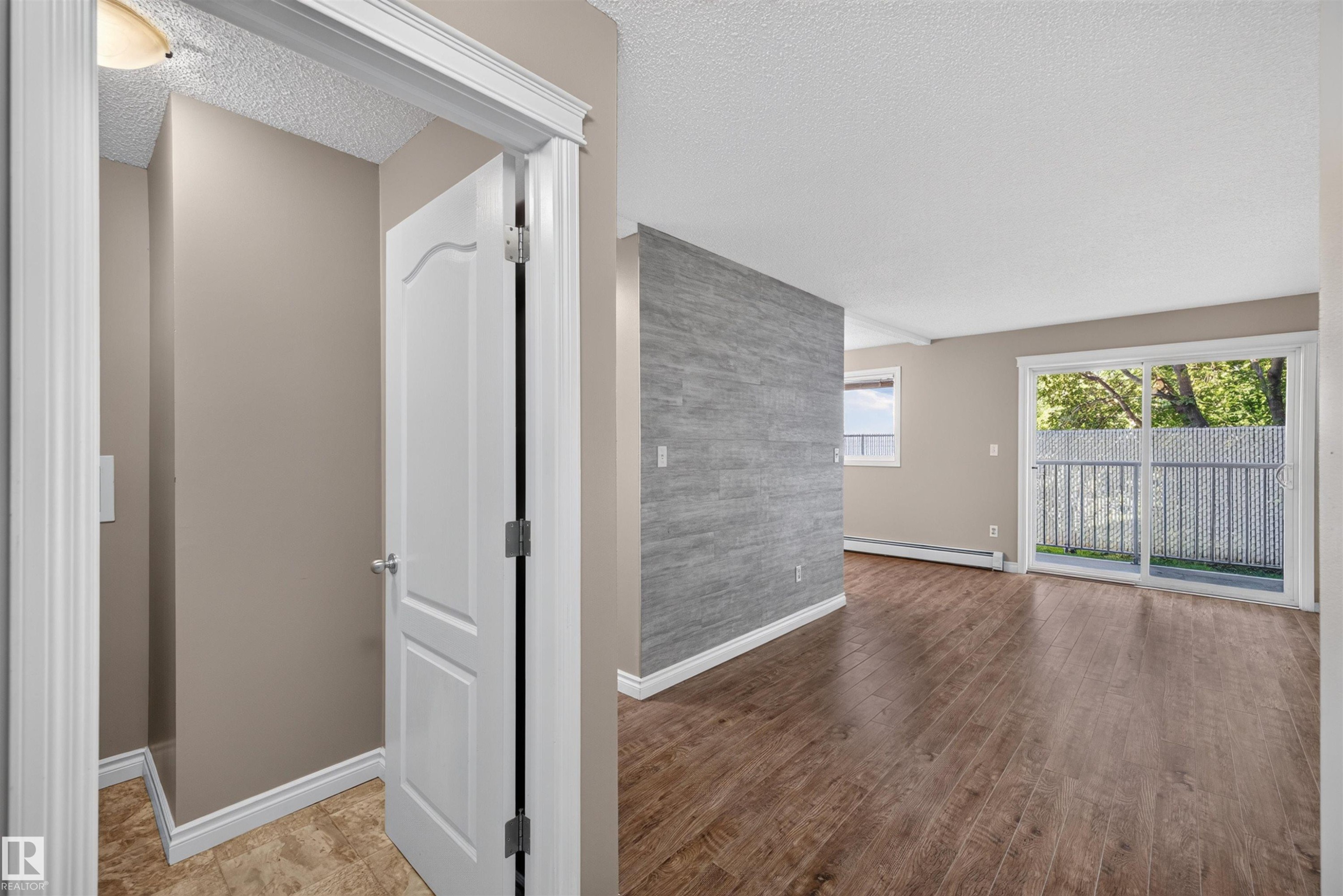 Hardwood-style flooring throughout, an accent wall with stacked stone-look tile, and a sliding glass door leading to an outdoor balcony - #4 4616 47 St, Leduc, AB - Indoor Photo Showing Other Room