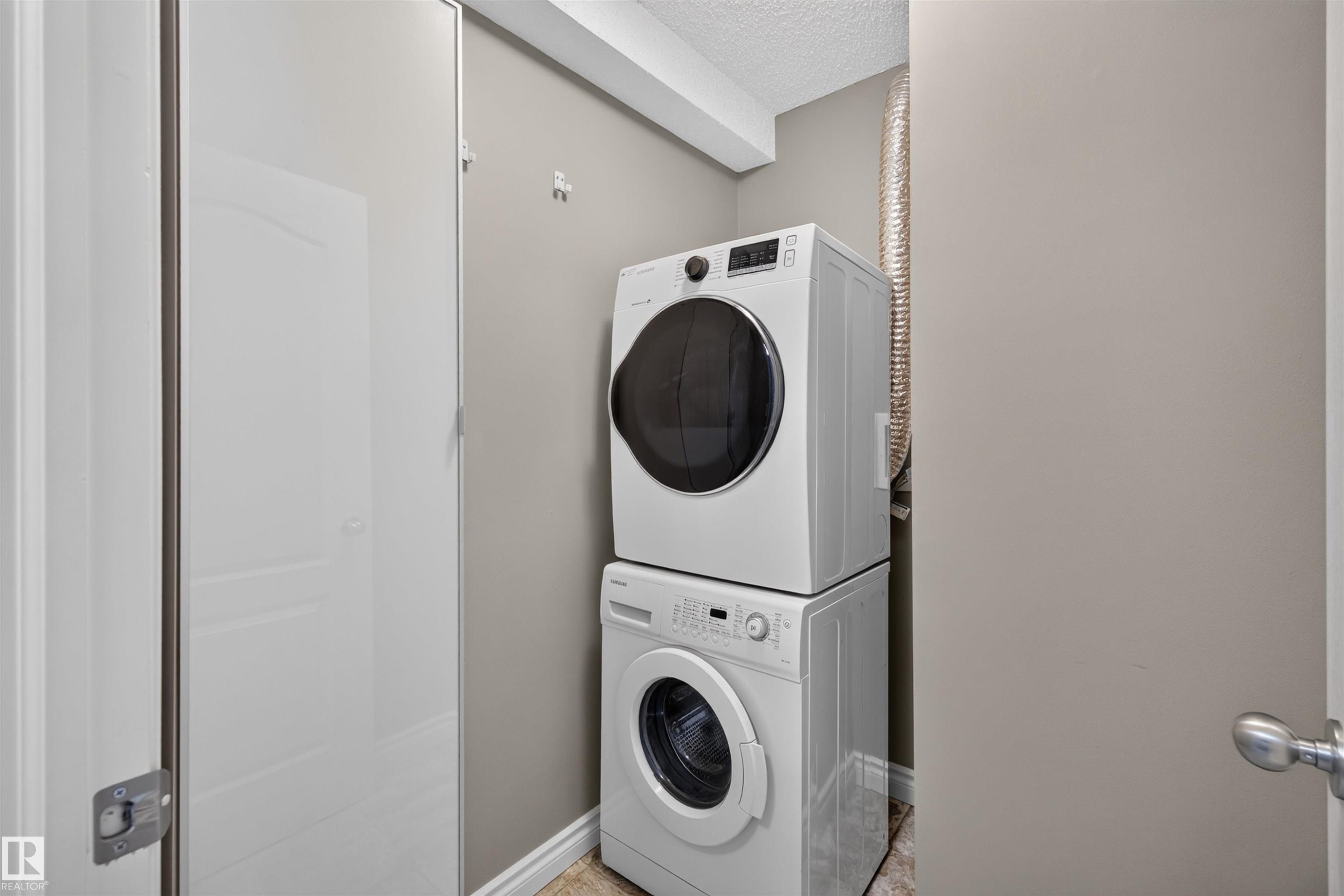 Stackable washer and dryer appliances, neutral wall paint, and wood-finish flooring - #4 4616 47 St, Leduc, AB - Indoor Photo Showing Laundry Room