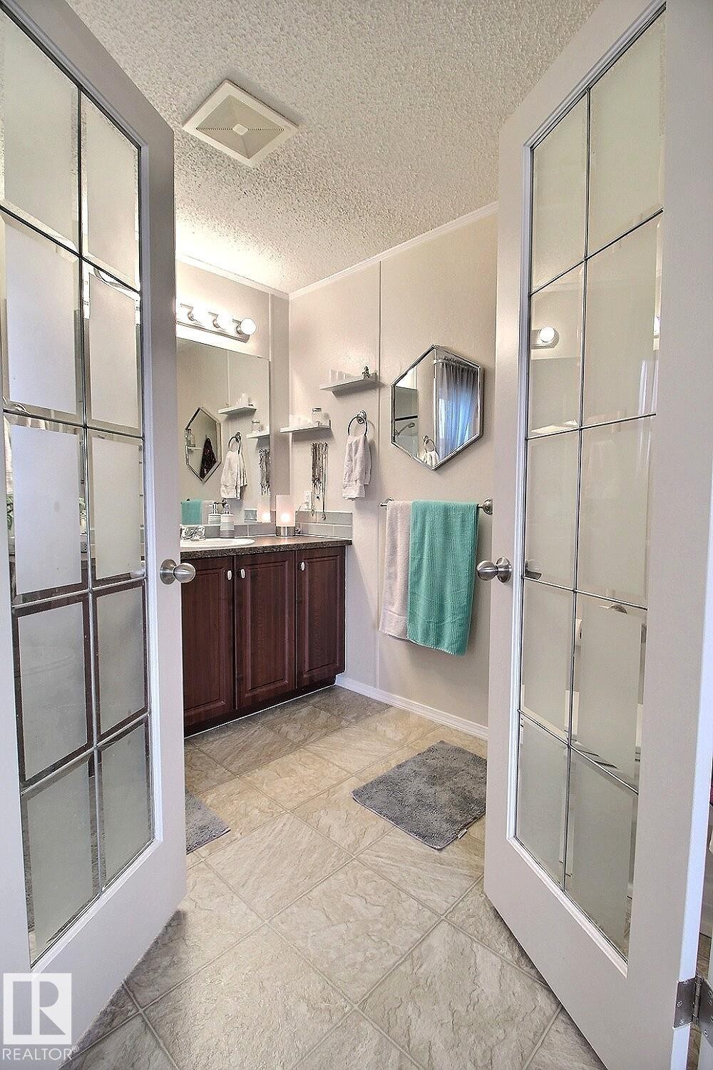 Bathroom featuring double French doors with frosted glass, a wood-finish vanity with an integrated sink, and an overhead vanity light fixture - 417 Oak Wood Crescent Northwest, Edmonton, AB - Indoor Photo Showing Other Room