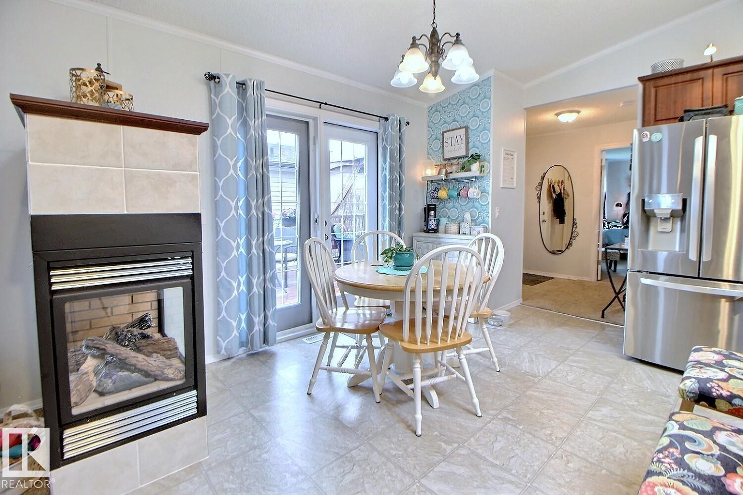 Tile-surround fireplace with a wood mantle, French doors, stainless steel refrigerator, and tiled flooring - 417 Oak Wood Crescent Northwest, Edmonton, AB - Indoor Photo Showing Dining Room With Fireplace