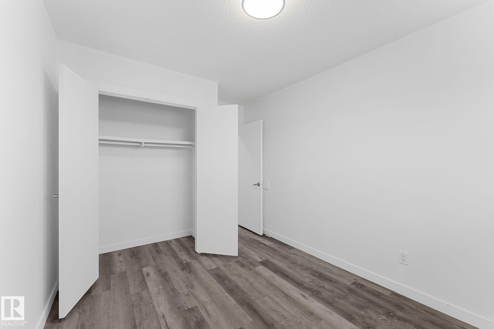 Recessed lighting fixture, wood-finish flooring, white walls, built-in closet with double hanging rods and shelf, white door with dark hardware - 7823 136 Avenue Nw, Edmonton, AB - Indoor Photo Showing Other Room