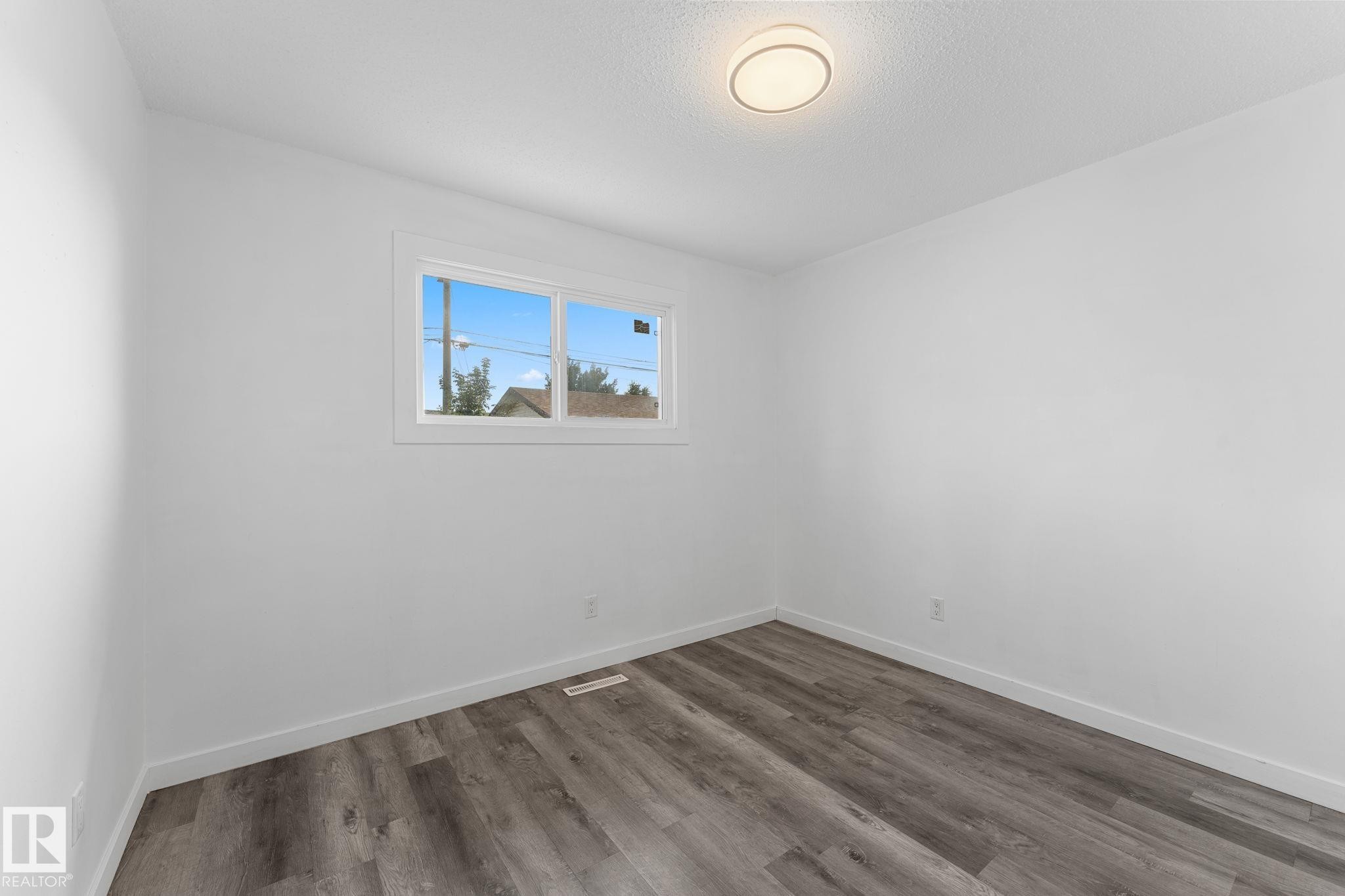 White walls, wood-finish flooring, and a flush mount ceiling light - 7823 136 Avenue Nw, Edmonton, AB - Indoor Photo Showing Other Room