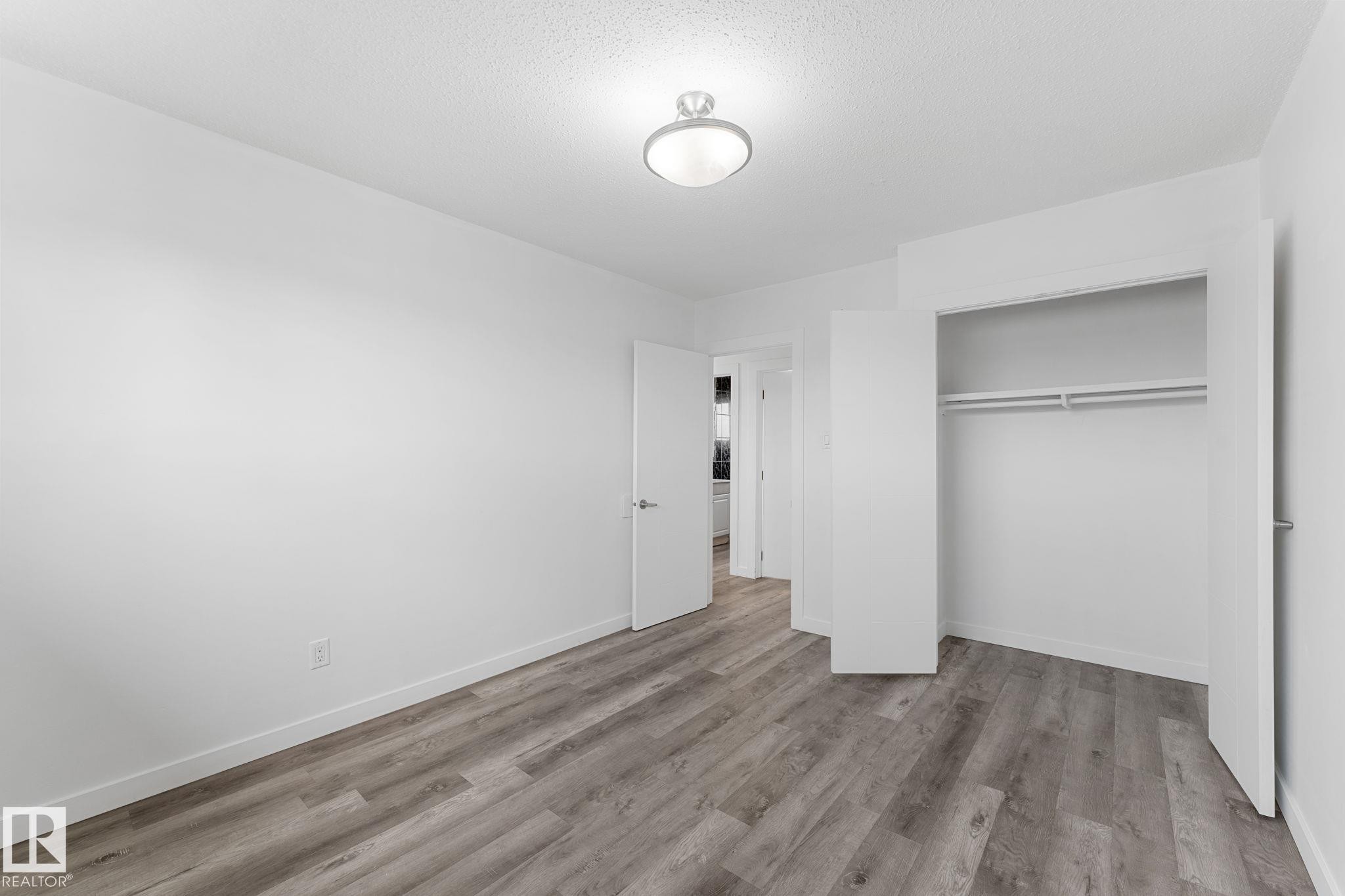 Wood-finish flooring, recessed ceiling light, white walls, double-door closet with hanging rods, and white trim - 7823 136 Avenue Nw, Edmonton, AB - Indoor Photo Showing Other Room