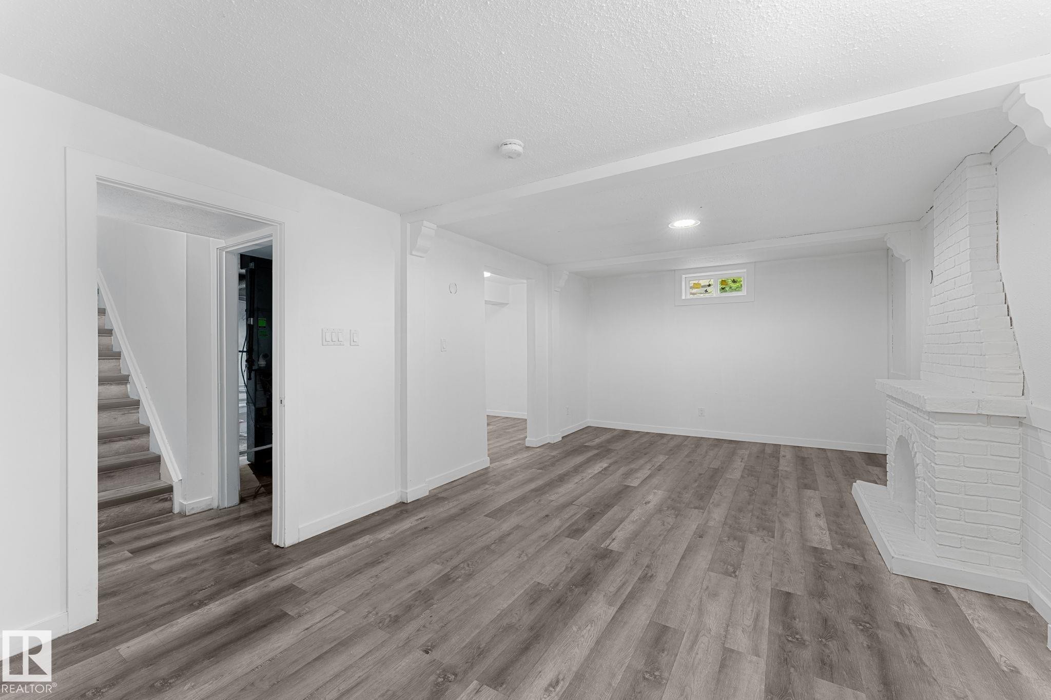 Spacious room featuring wood-finish flooring, white painted brick fireplace, and recessed lighting - 7823 136 Avenue Nw, Edmonton, AB - Indoor